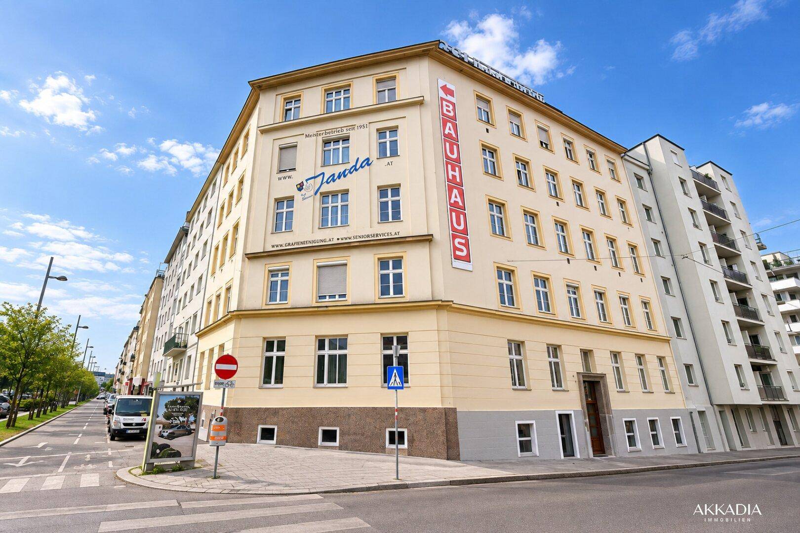Mehrstöckiges Eckgebäude mit cremefarbener Fassade und vielen Fenstern an einer Stadtstraße.