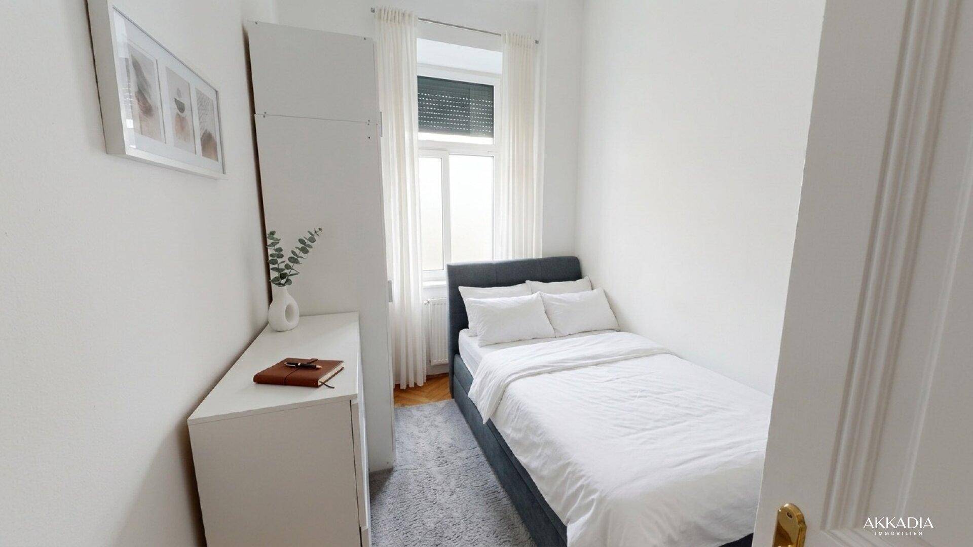 Kleines, helles Schlafzimmer mit Einzelbett, weißem Kleiderschrank und Fenster.