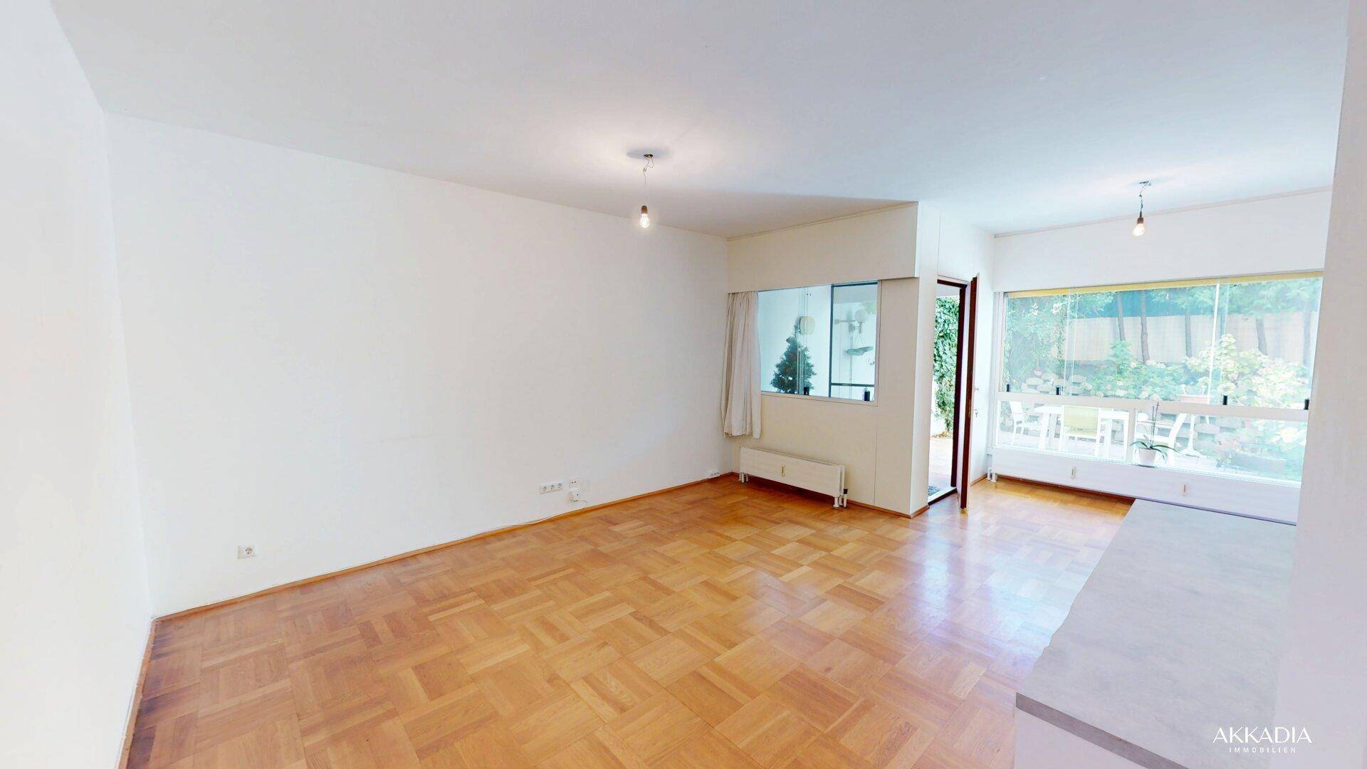 Geräumiges Wohnzimmer mit Parkettboden und Zugang zu einem verglasten Außenbereich.