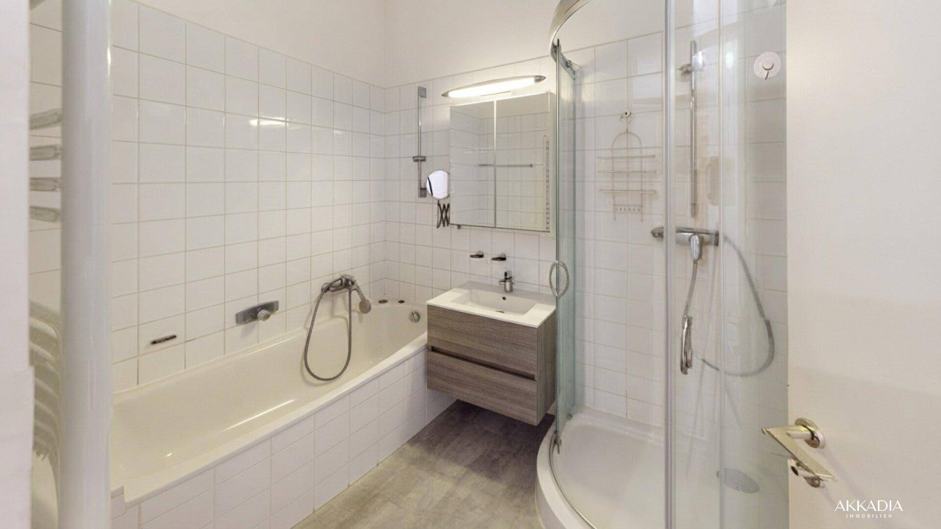 Helles Badezimmer mit Badewanne, Duschkabine, Waschtisch und weißen Wandfliesen.