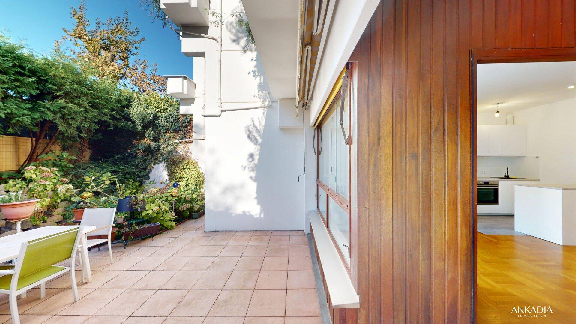 Sonniger Terrassenbereich mit Holzwand und Blick in den offenen Wohnbereich der Wohnung.