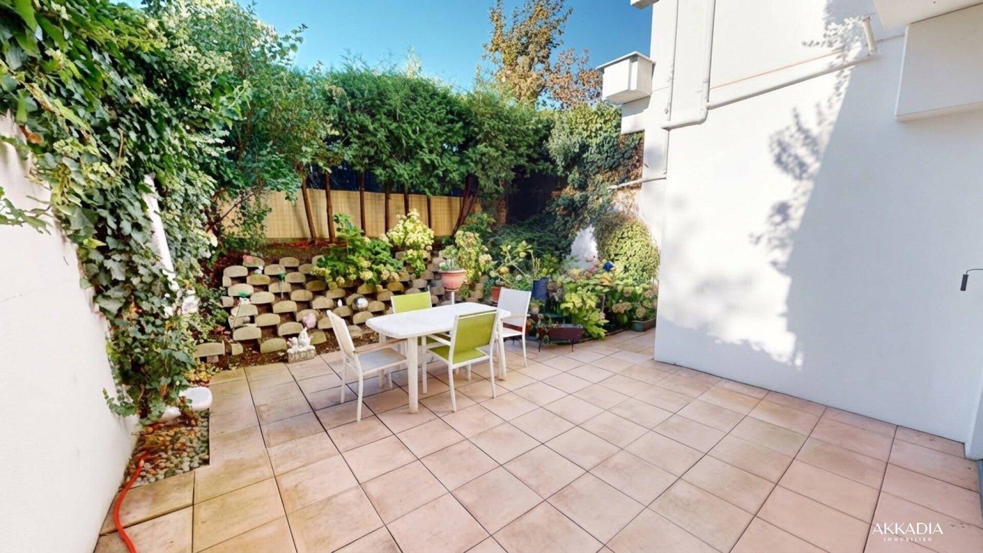Geflieste Terrasse mit Gartenmöbeln und üppiger grüner Bepflanzung im Hintergrund.