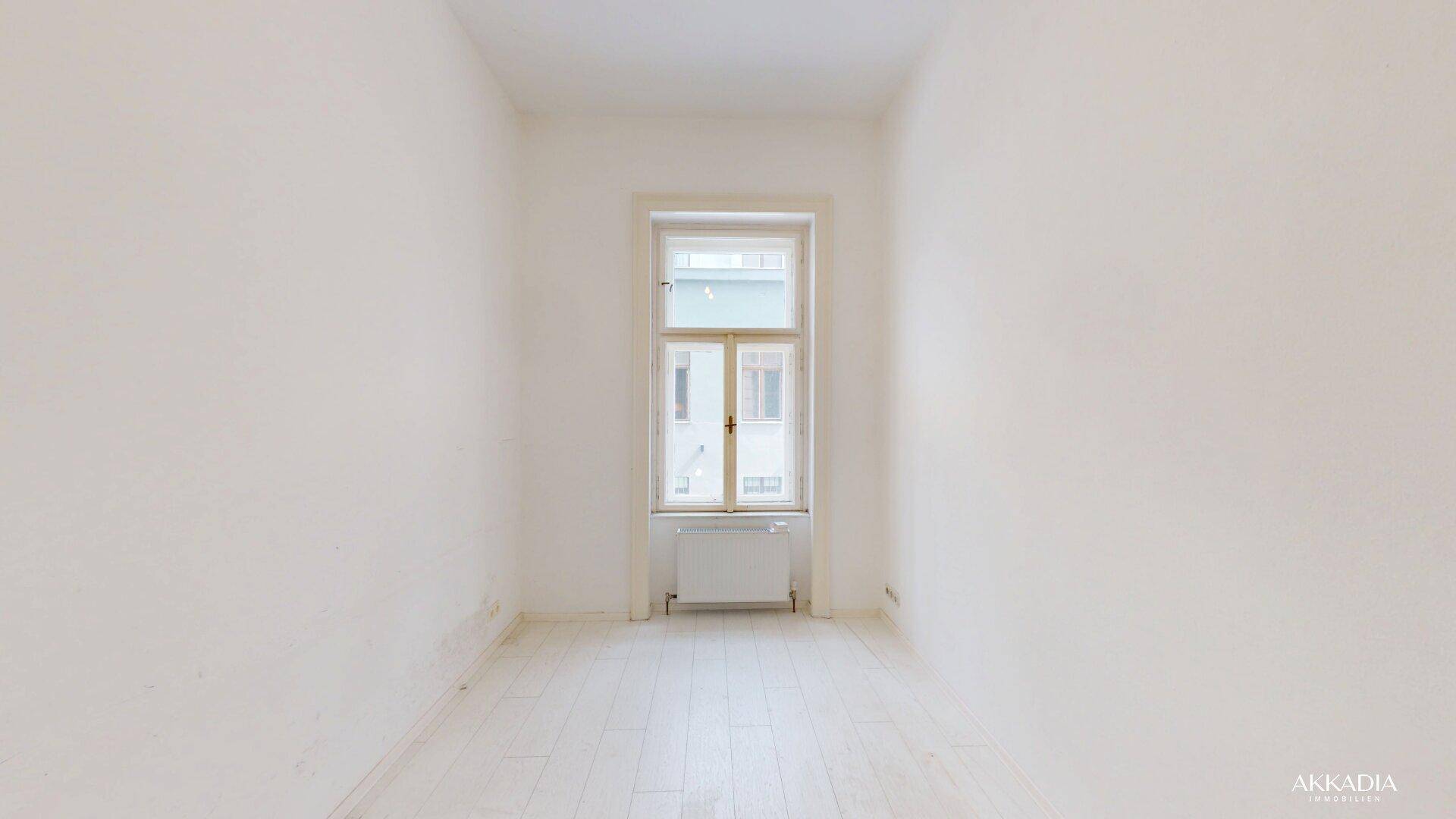Schmaler, heller Raum mit einem großen Fenster, hohen Decken und hellem Dielenboden, vielseitig nutzbar.
