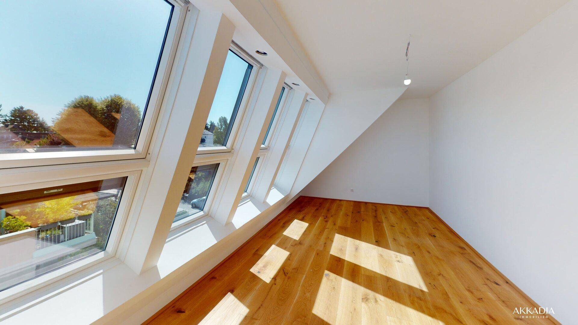 Heller Raum mit Holzboden und einer Reihe von Dachfenstern, die viel Tageslicht bieten.