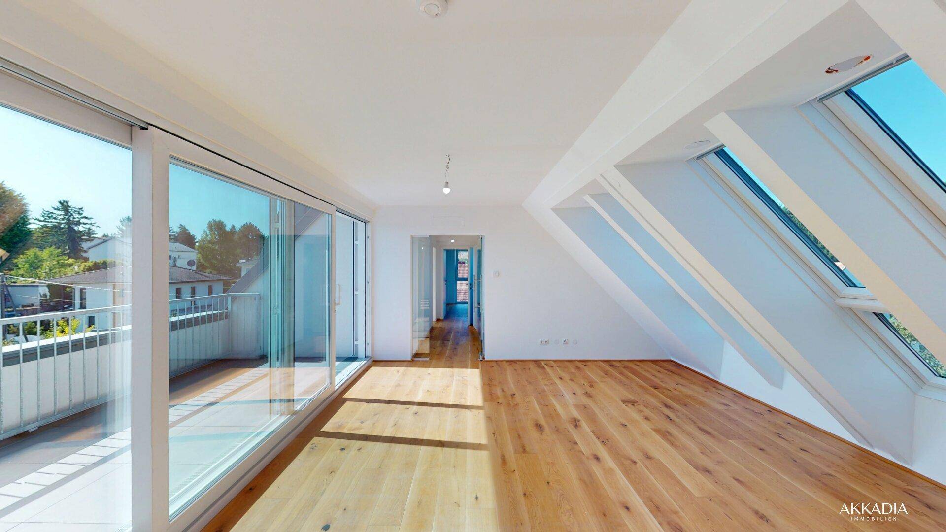 Geräumiges Zimmer mit Holzboden, Schiebetüren zum Balkon und schrägen Dachfenstern.