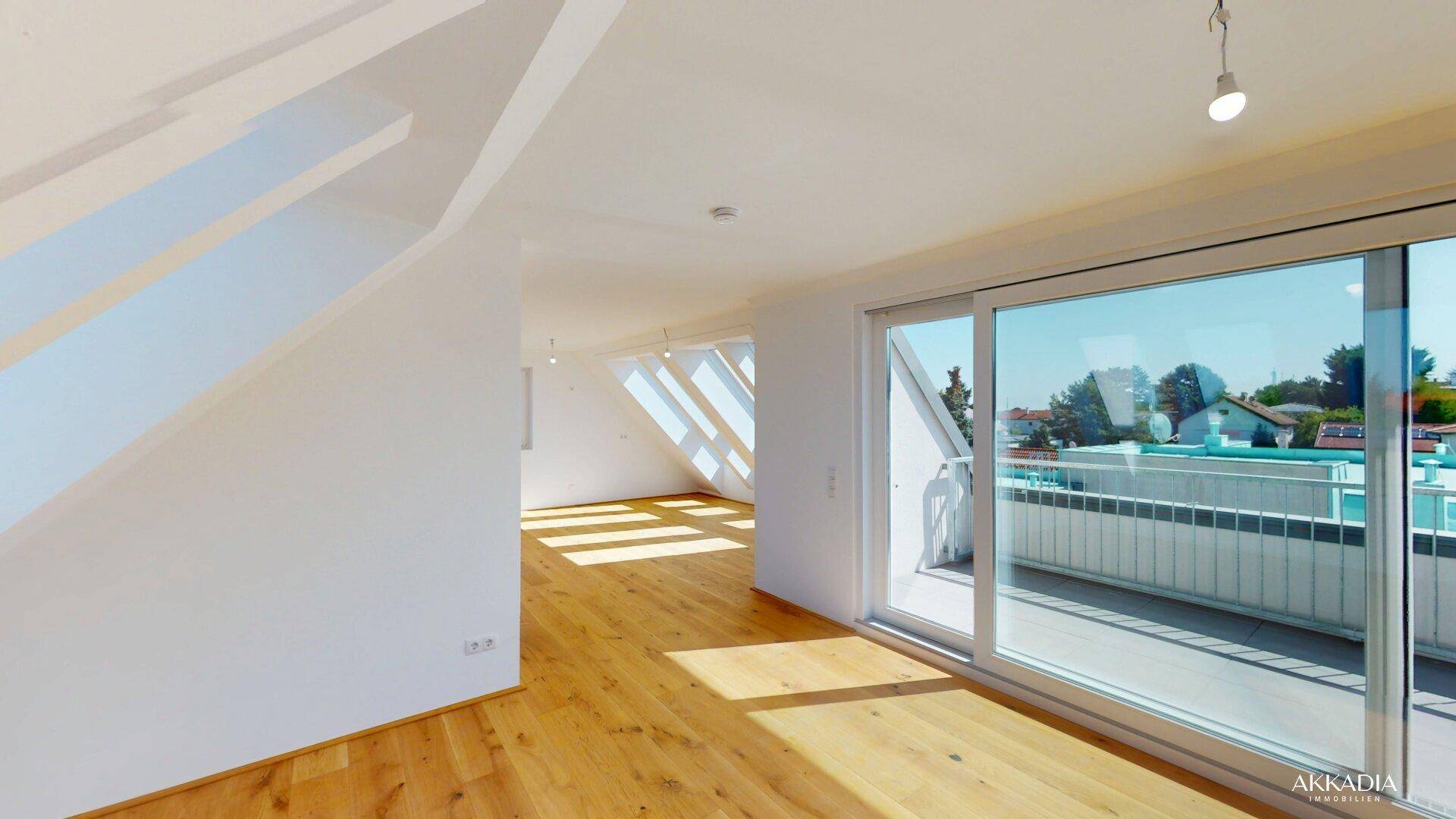 Heller Raum mit Holzboden, schrägen Wänden und Zugang zu einem sonnigen Balkon.