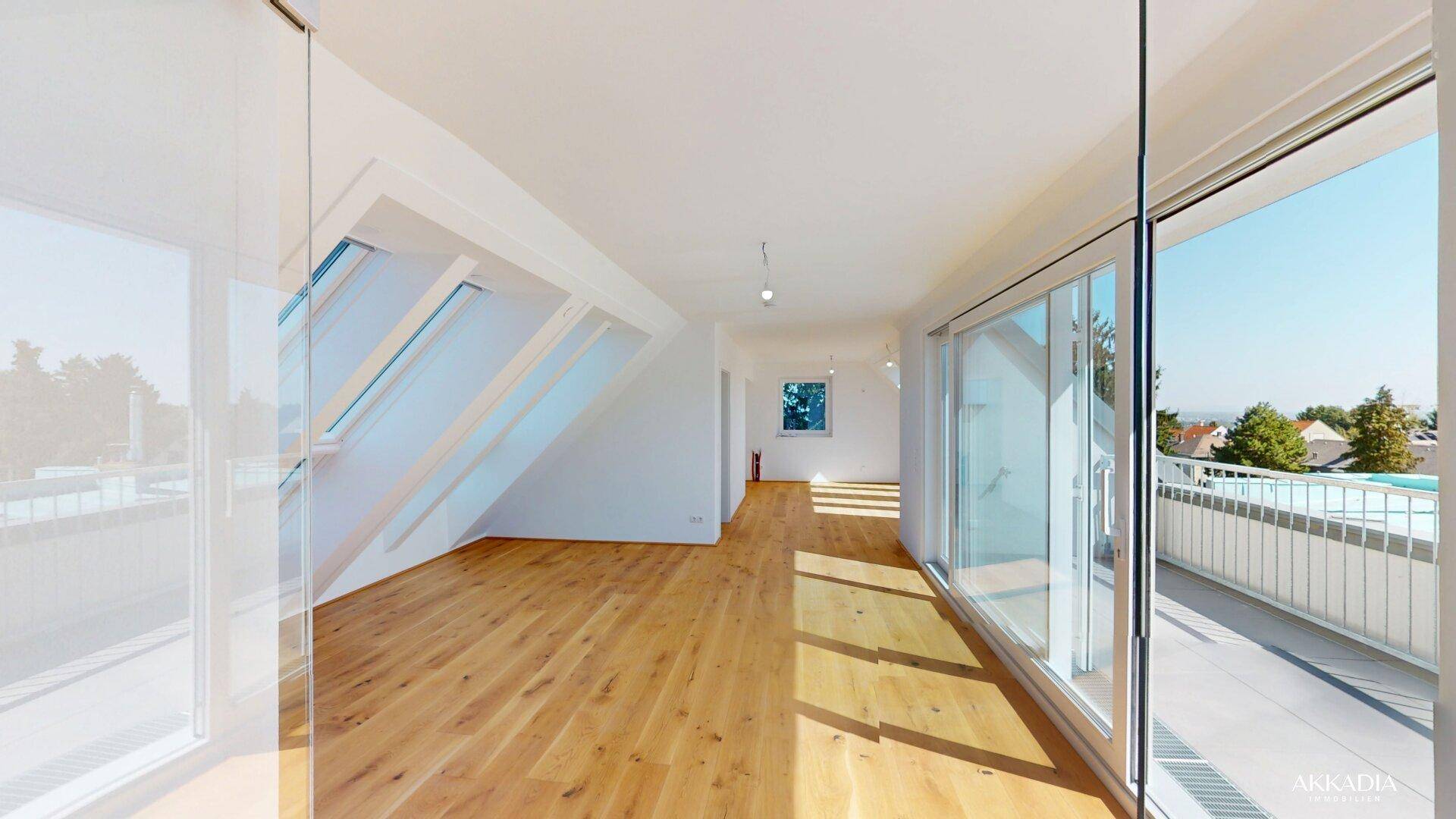 Geräumiger, heller Raum mit Holzboden, großen Glasfronten und Zugang zu einem Balkon.
