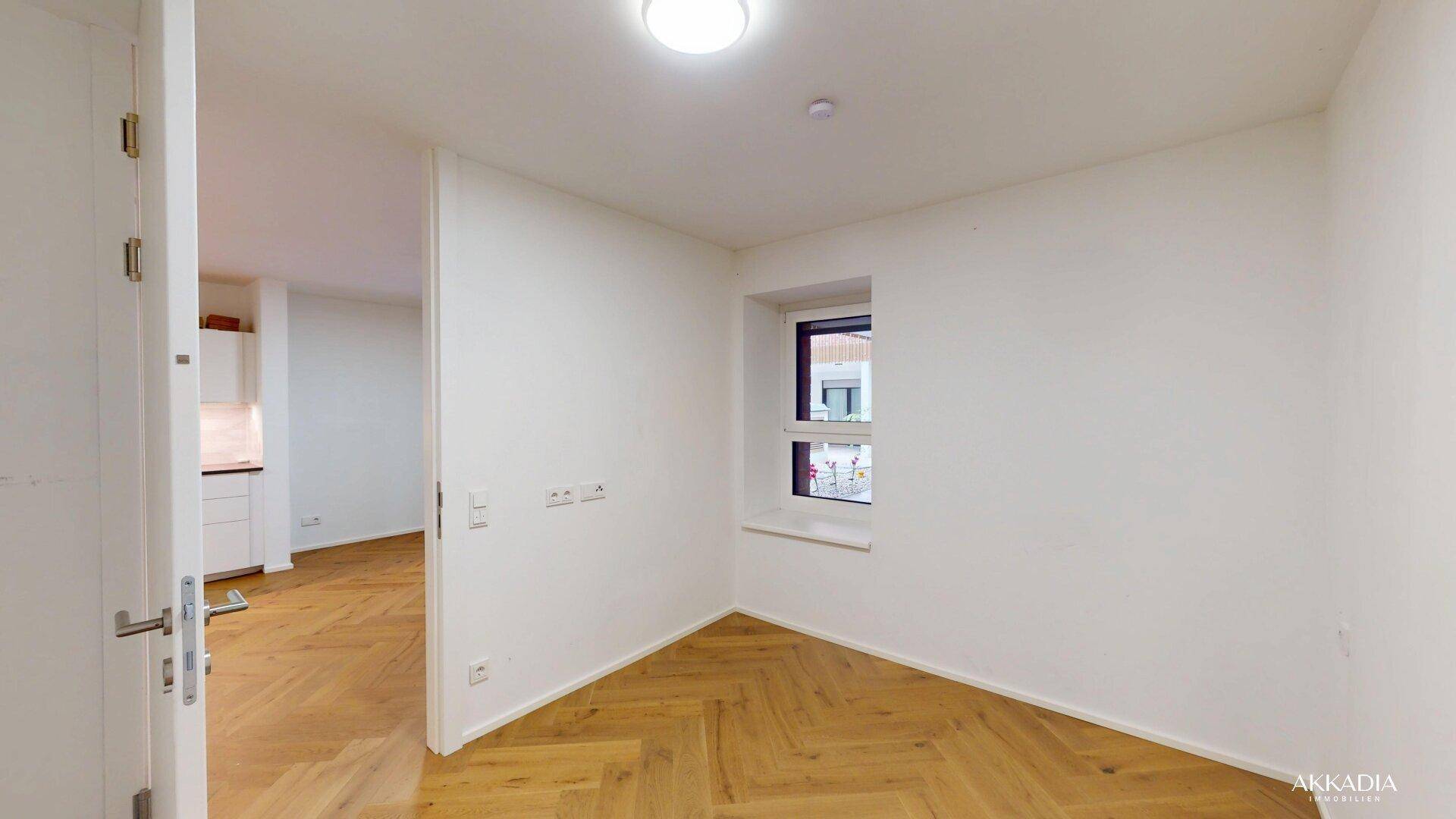 Helles Zimmer mit Fischgrätparkett und einem Fenster zum Innenhof.