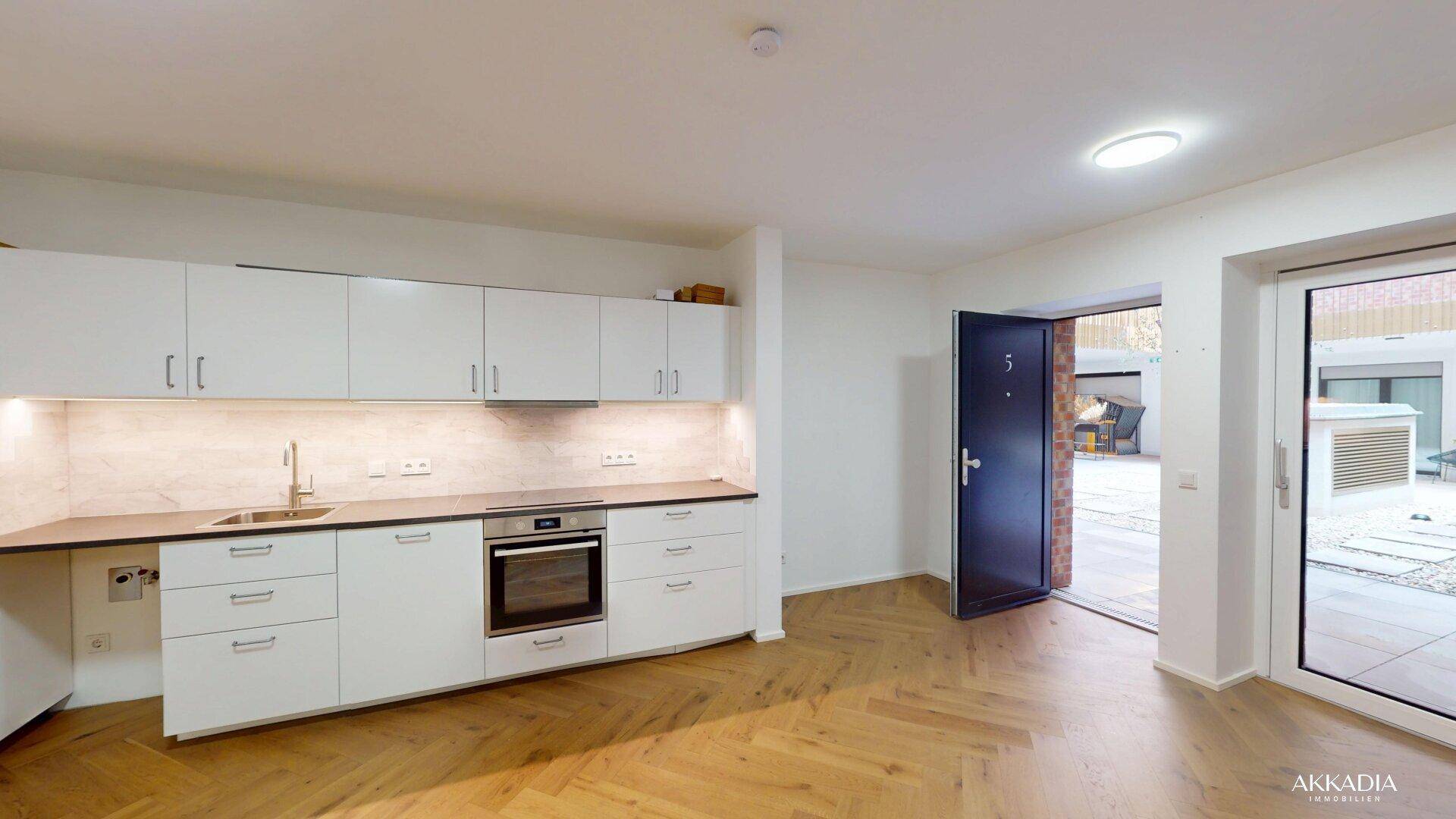 Moderne Küchenzeile mit weißen Schränken, integriertem Backofen und Fischgrätparkett.