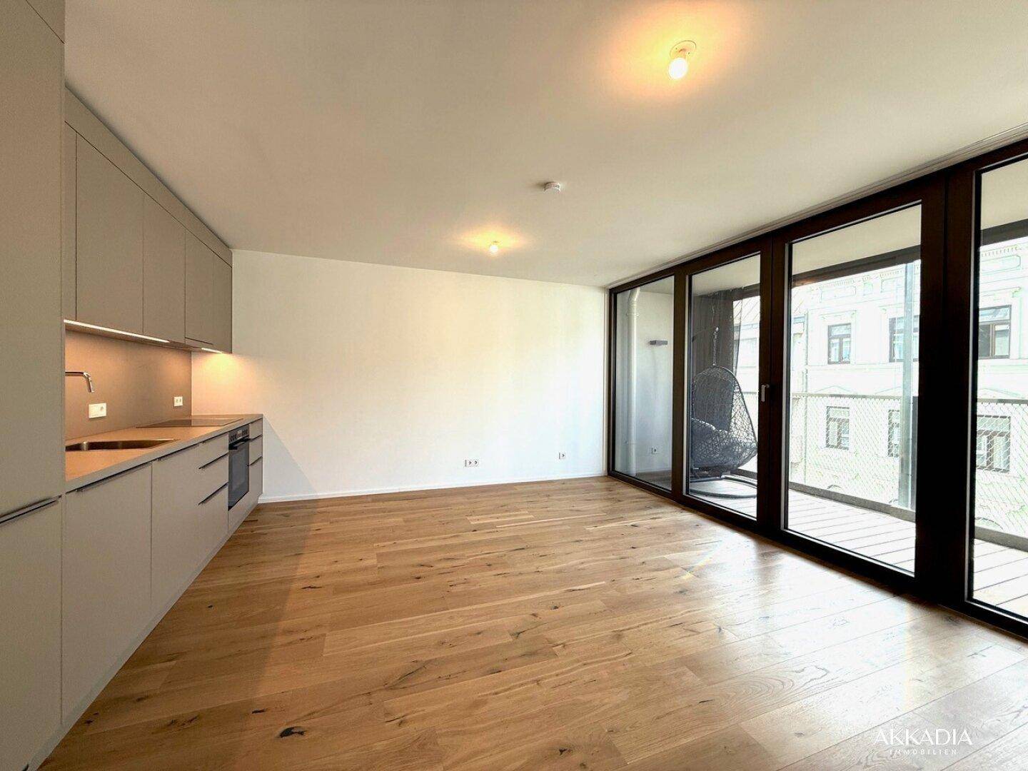 Offener Wohnbereich mit integrierter Küche, Holzboden und Zugang zum Balkon.