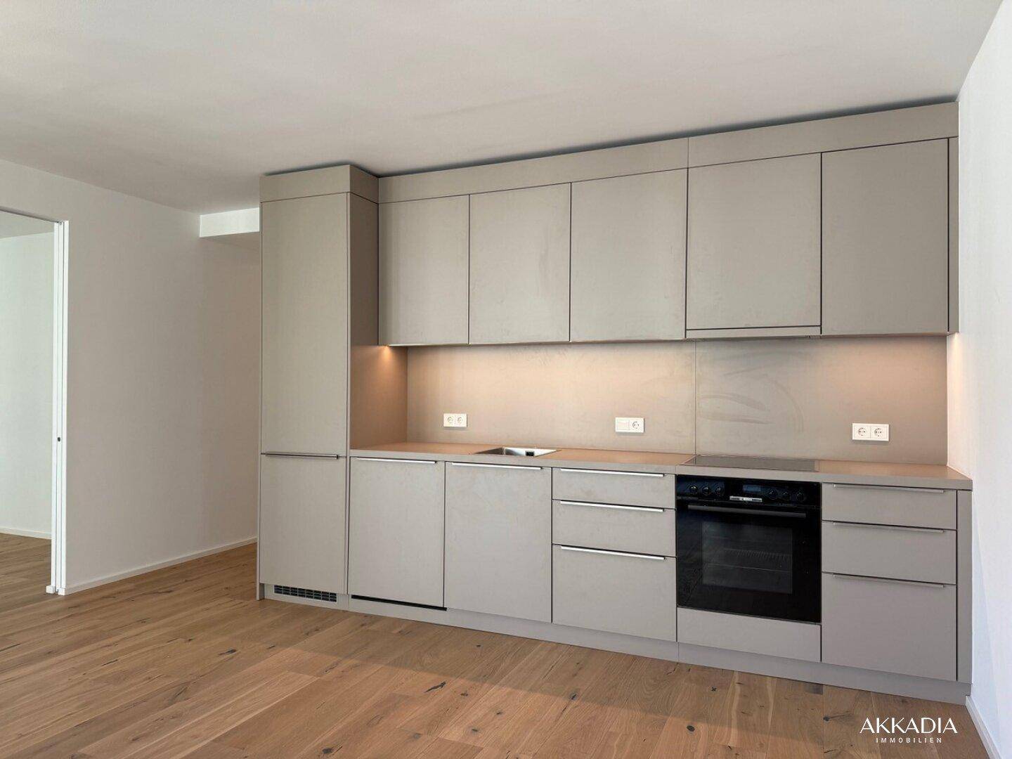 Moderne Einbauküche in hellem Grau mit integrierten Geräten und Holzboden.