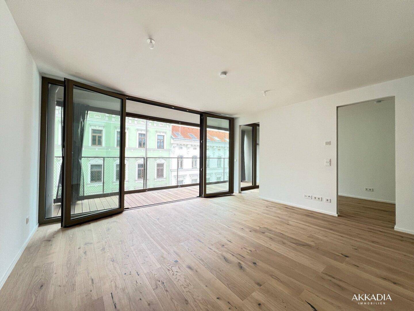 Heller Wohnraum mit großen Glasfronten, Holzboden und Zugang zu einem Balkon.
