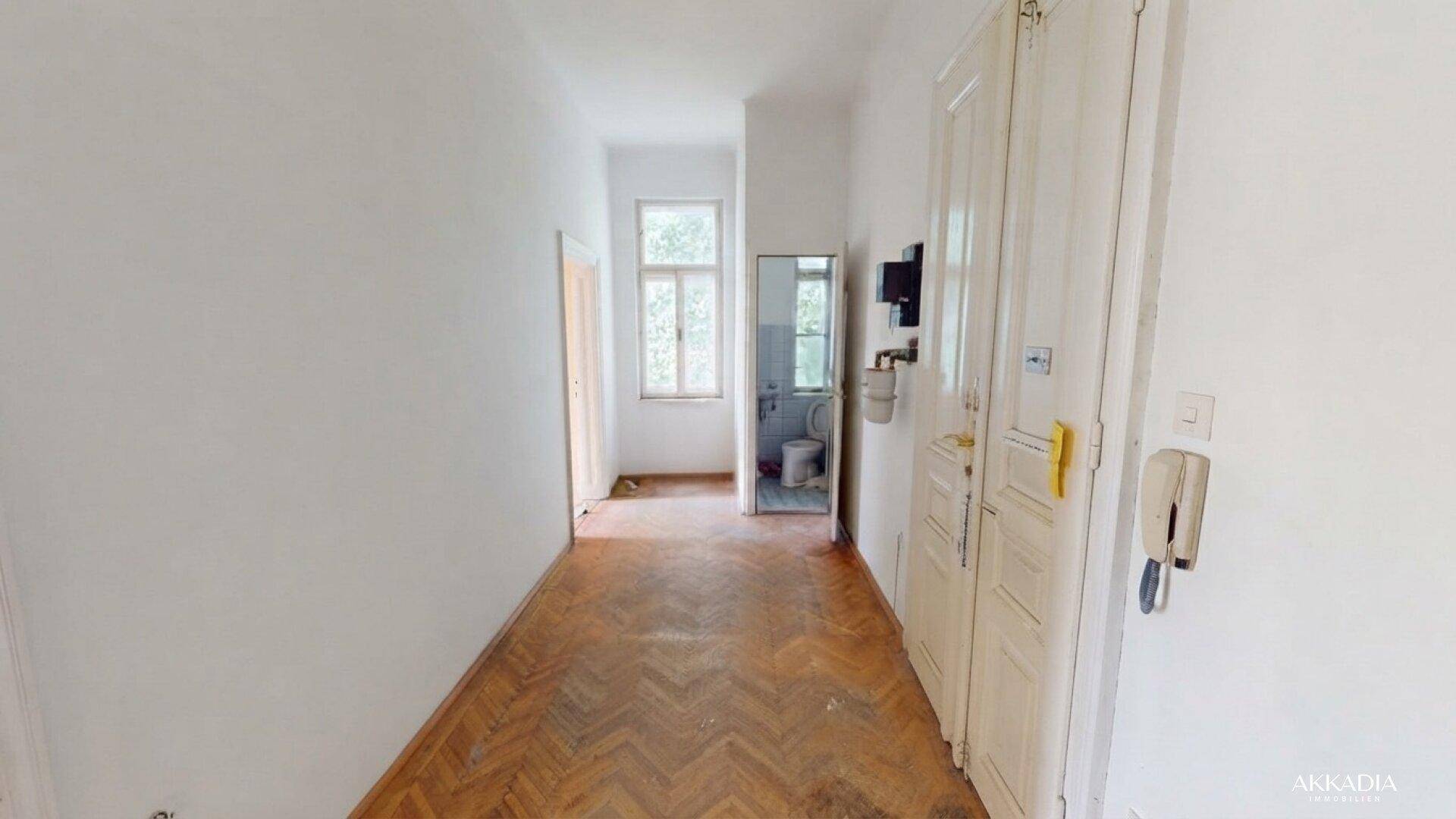Langer Flur mit Fischgrätparkett und Zugang zu einem Badezimmer sowie weiteren Räumen.
