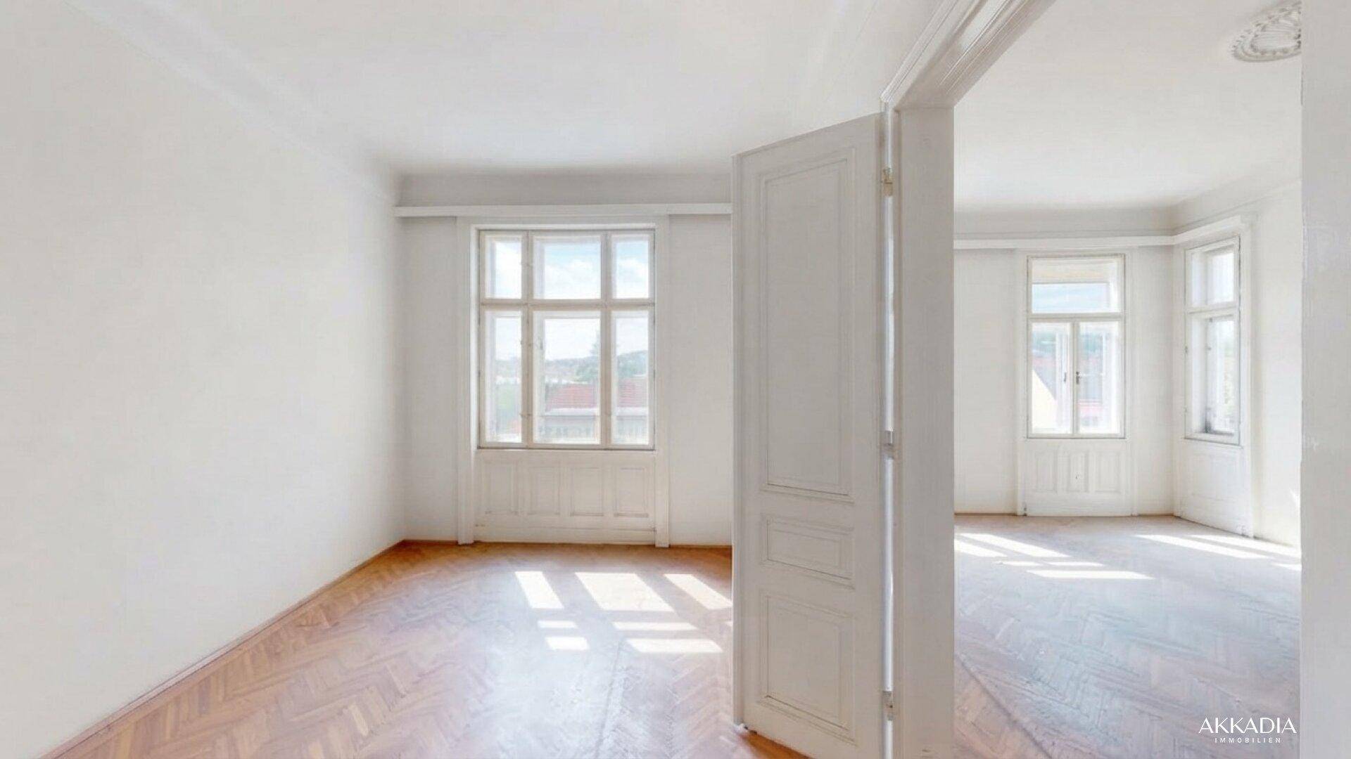 Geräumiges, helles Zimmer mit Fischgrätparkett und Blick ins Grüne durch die großen Fenster.