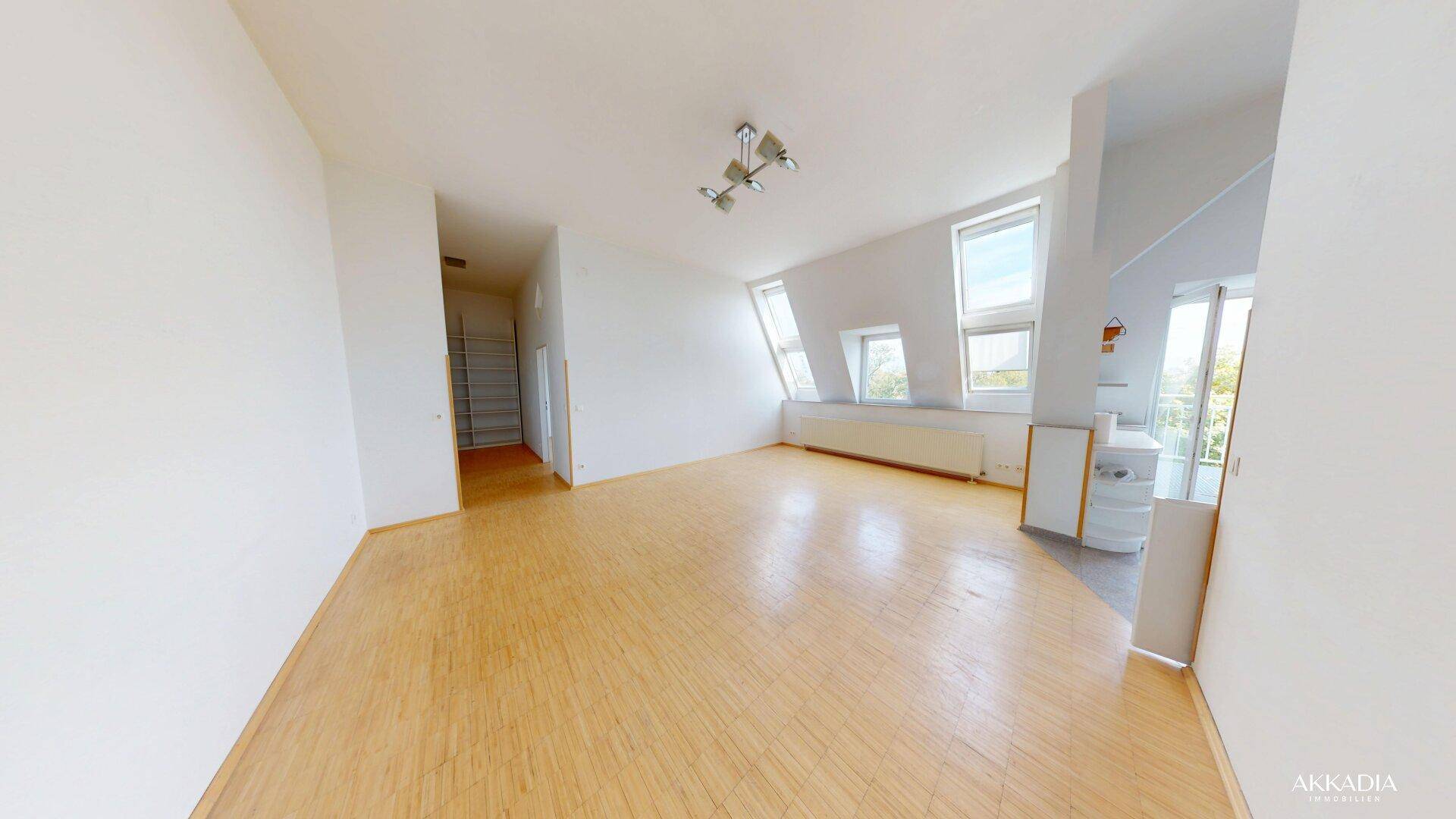 Heller Wohnraum im Dachgeschoss mit Holzfußboden, schrägen Wänden und Dachfenstern.