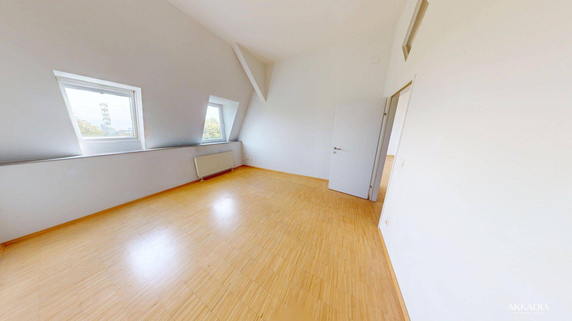 Weiteres helles Schlafzimmer im Dachgeschoss mit Holzfußboden und Dachfenstern.
