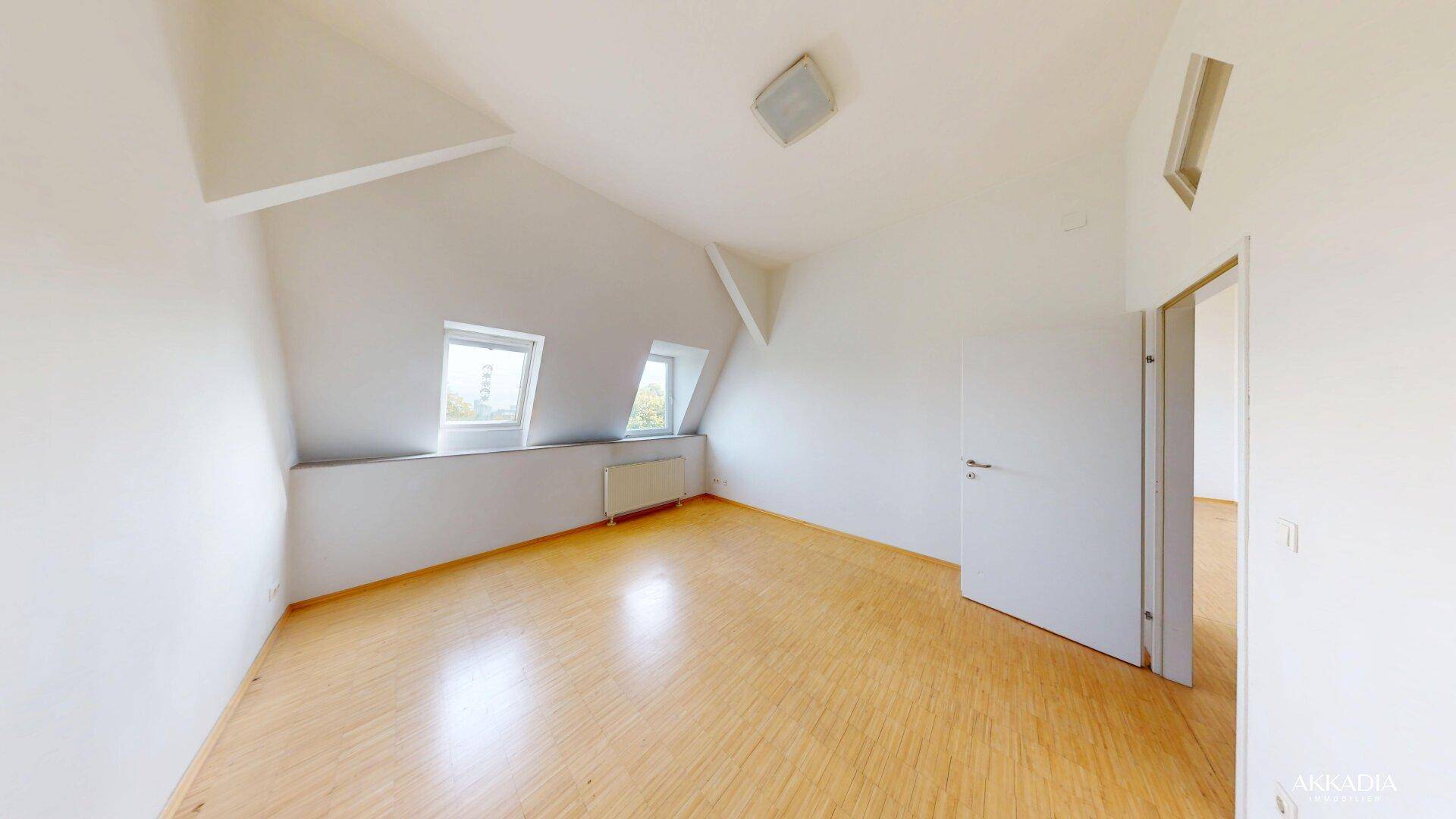 Helles Schlafzimmer im Dachgeschoss mit Holzfußboden, schrägen Wänden und Dachfenstern.