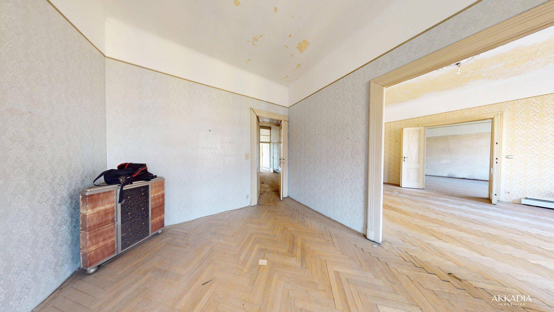 Leeres Zimmer mit Fischgrätparkett und Tapetenresten, das auf eine Modernisierung wartet.