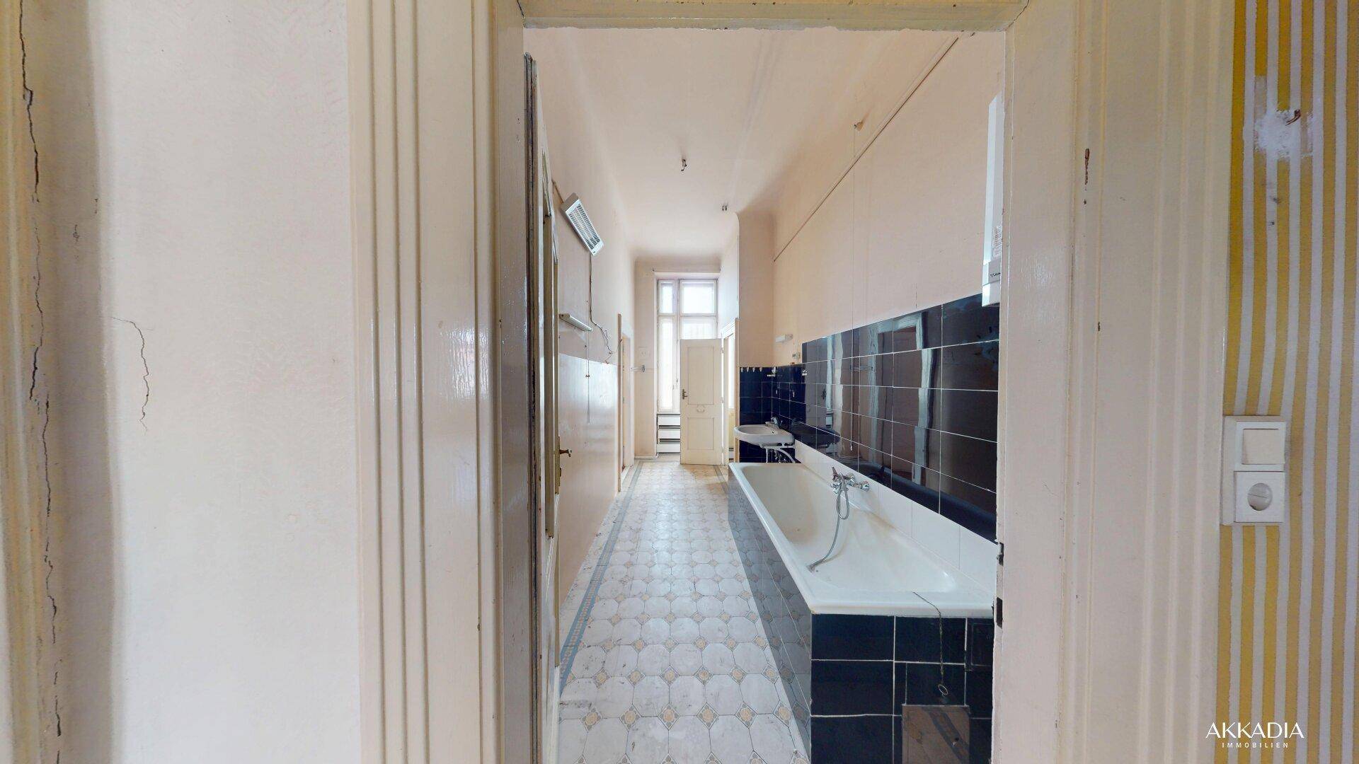 Langes Badezimmer mit Badewanne und Fliesenboden, das eine Modernisierung benötigt.