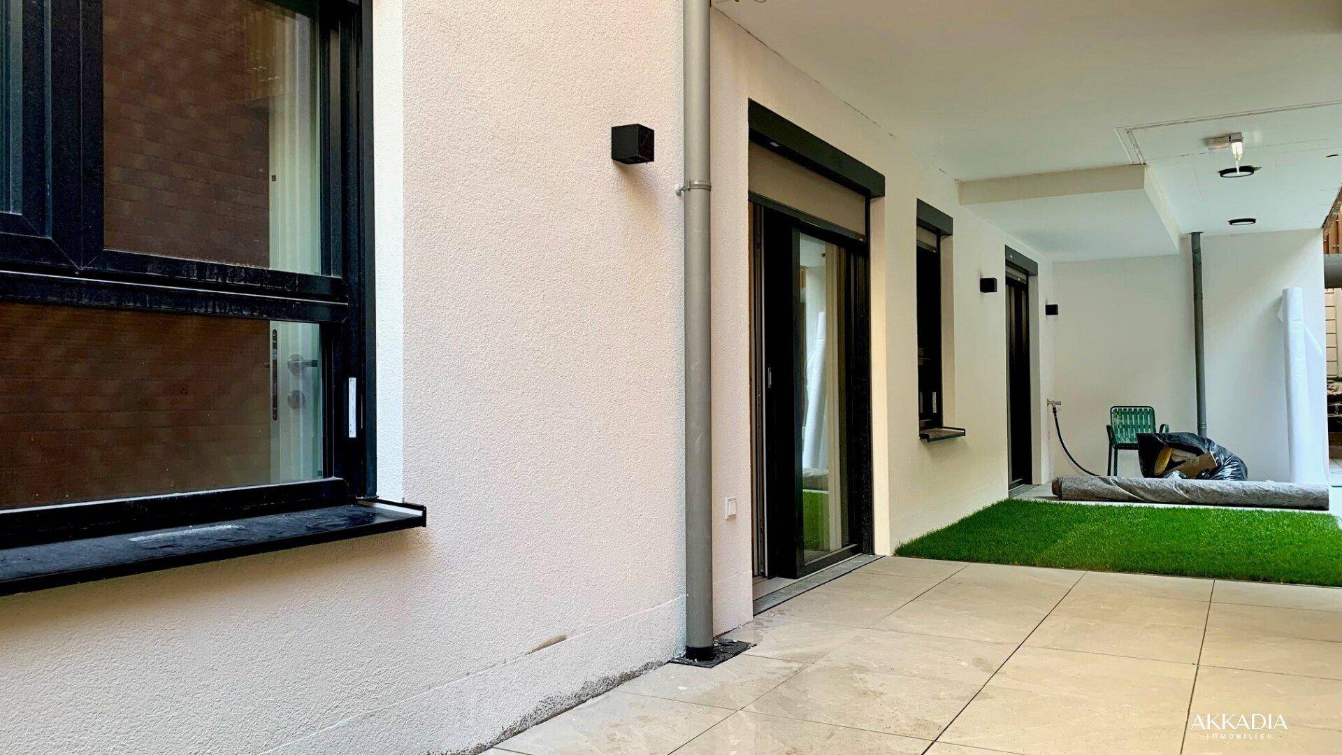 Außenbereich mit gepflasterter Terrasse, Rasenstreifen und großen Schiebetüren zum Innenraum.