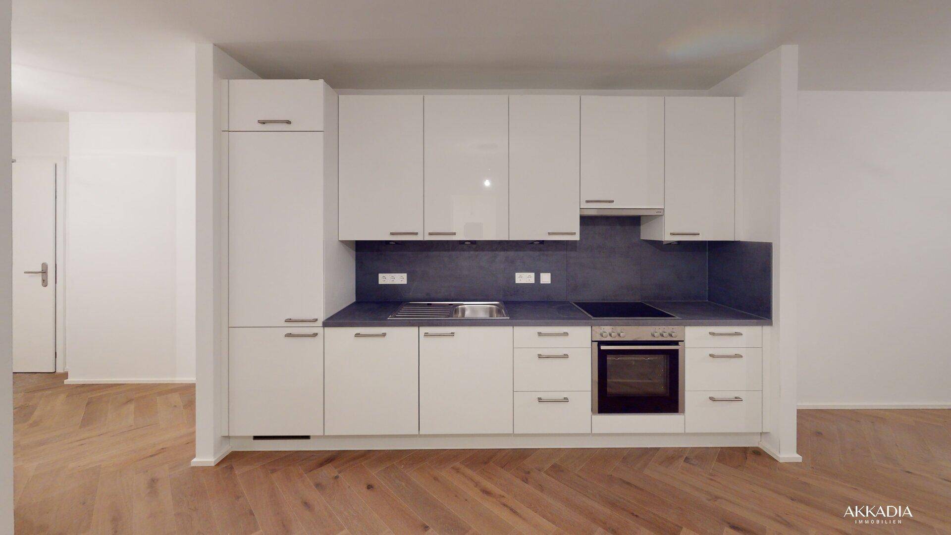 Moderne Einbauküche mit weißen Hochglanzfronten, dunkler Arbeitsplatte und integrierten Geräten.