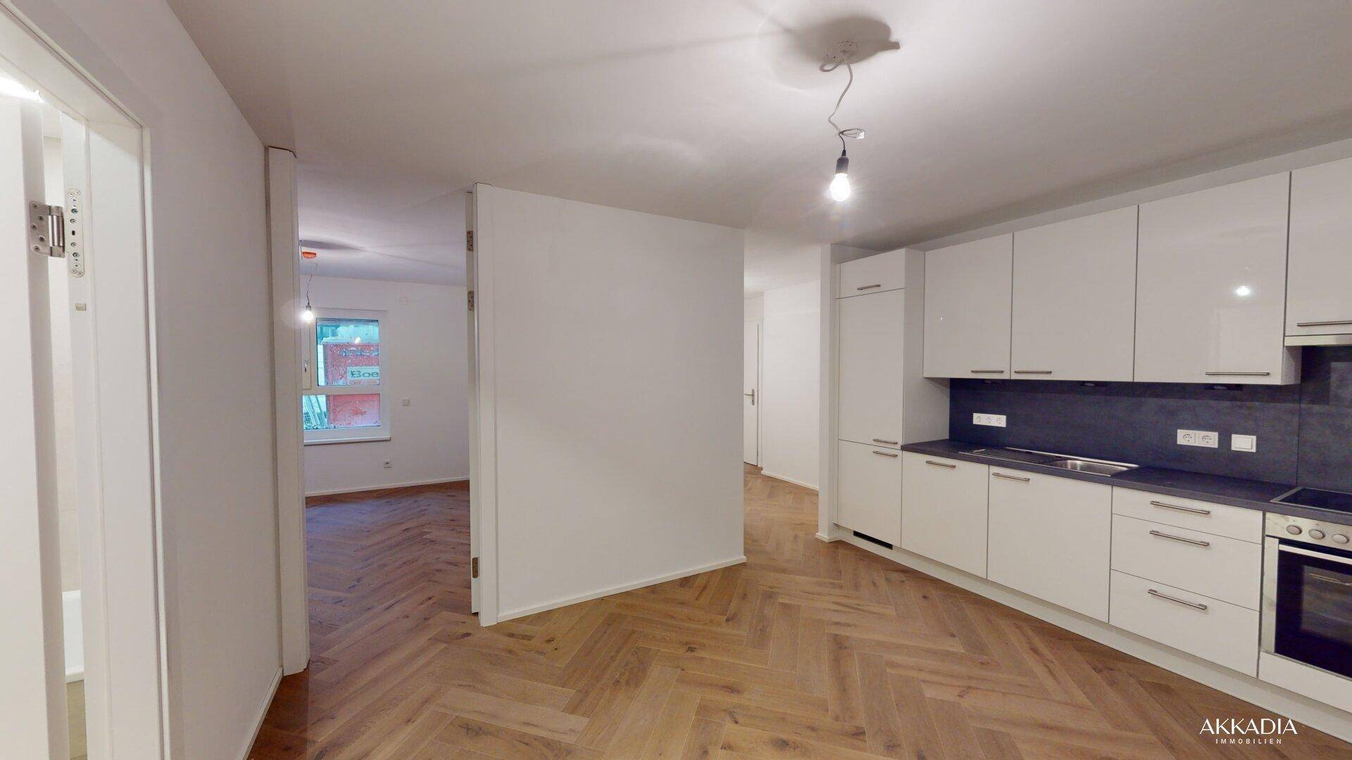 Offene Küche mit weißen Hochglanzschränken und Fischgrätparkett, Blick in den Wohnbereich.