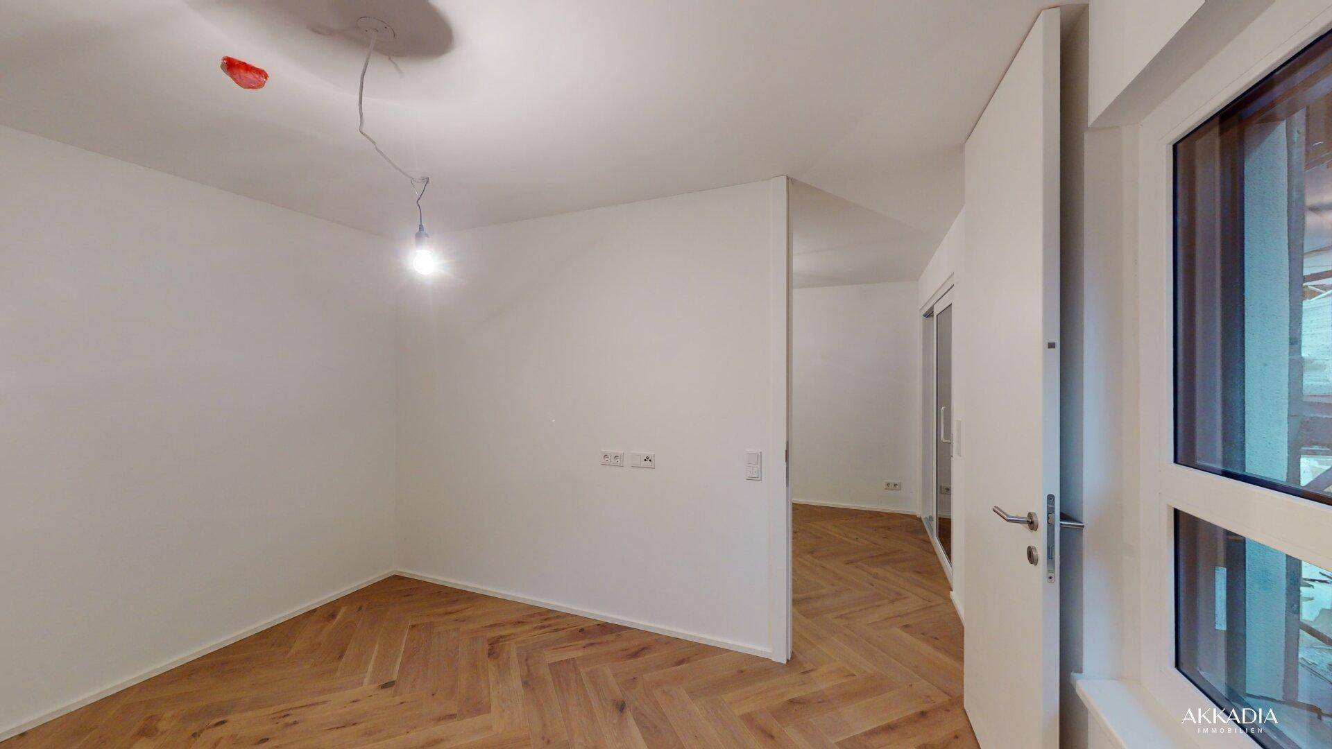 Helles Zimmer mit Fischgrätparkett und weiß gestrichenen Wänden, mit Blick nach draußen.