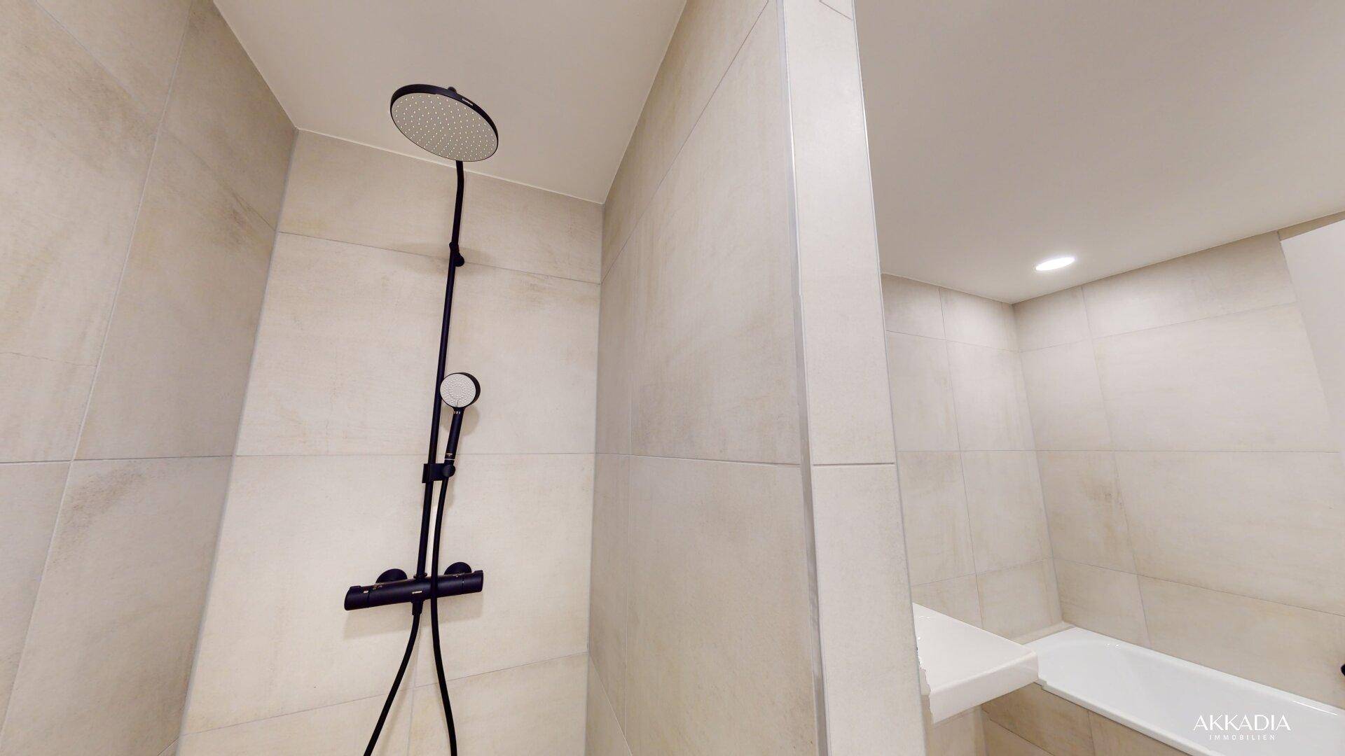 Moderne Dusche mit schwarzen Armaturen und hellen, großformatigen Wandfliesen.