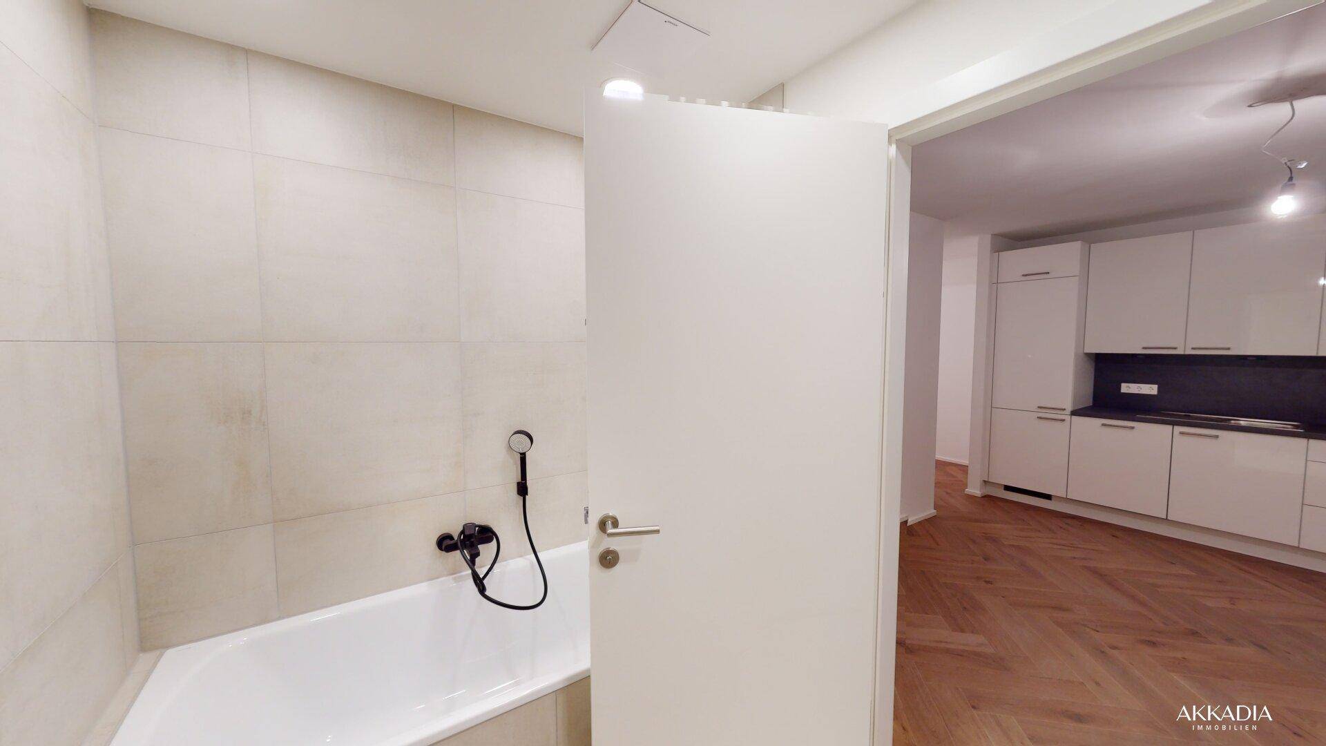 Modernes Badezimmer mit Badewanne und hellen Fliesen, offener Blick zur Küche.