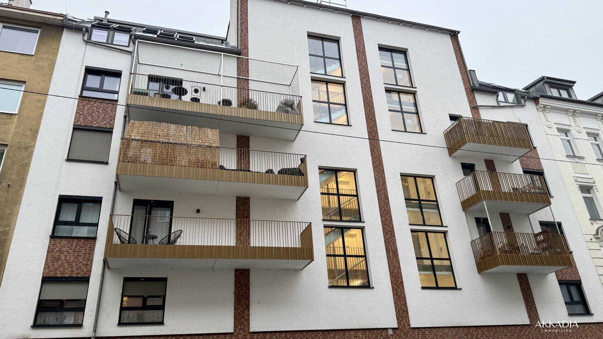 Moderne Wohnhausfassade mit Balkonen, großen Fenstern und Ziegelakzenten unter bewölktem Himmel.
