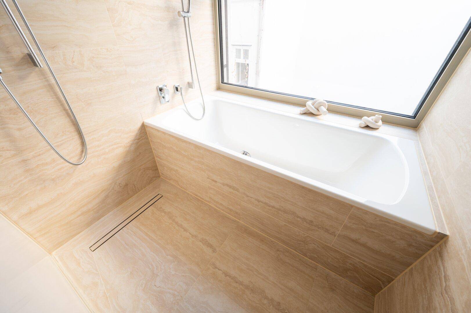 Geräumiges Badezimmer mit Badewanne, integrierter Dusche und Fenster für natürliche Belüftung.