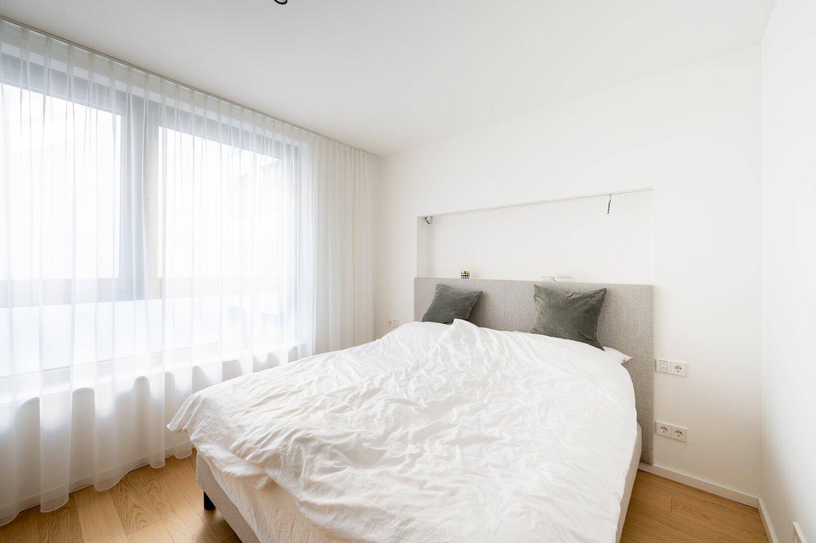 Helles Schlafzimmer mit großem Bett, viel Tageslicht und minimalistischer Einrichtung.