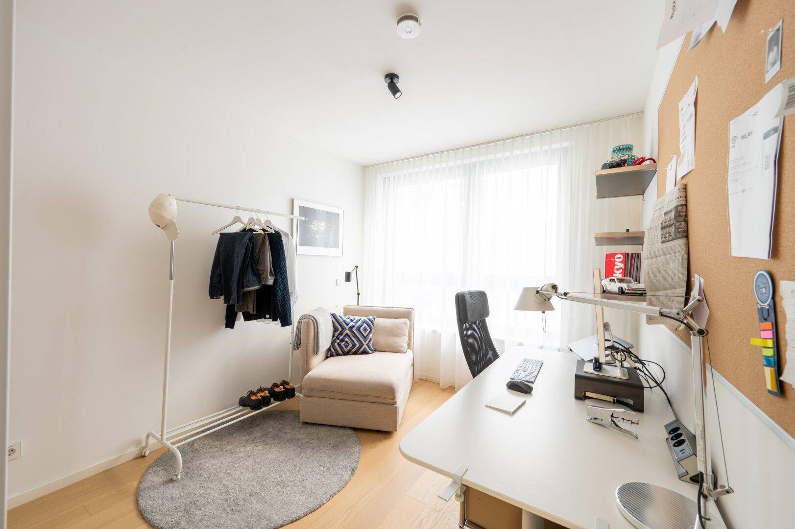 Funktionaler Arbeitsbereich mit Schreibtisch, Bürostuhl und viel Tageslicht durch große Fenster.