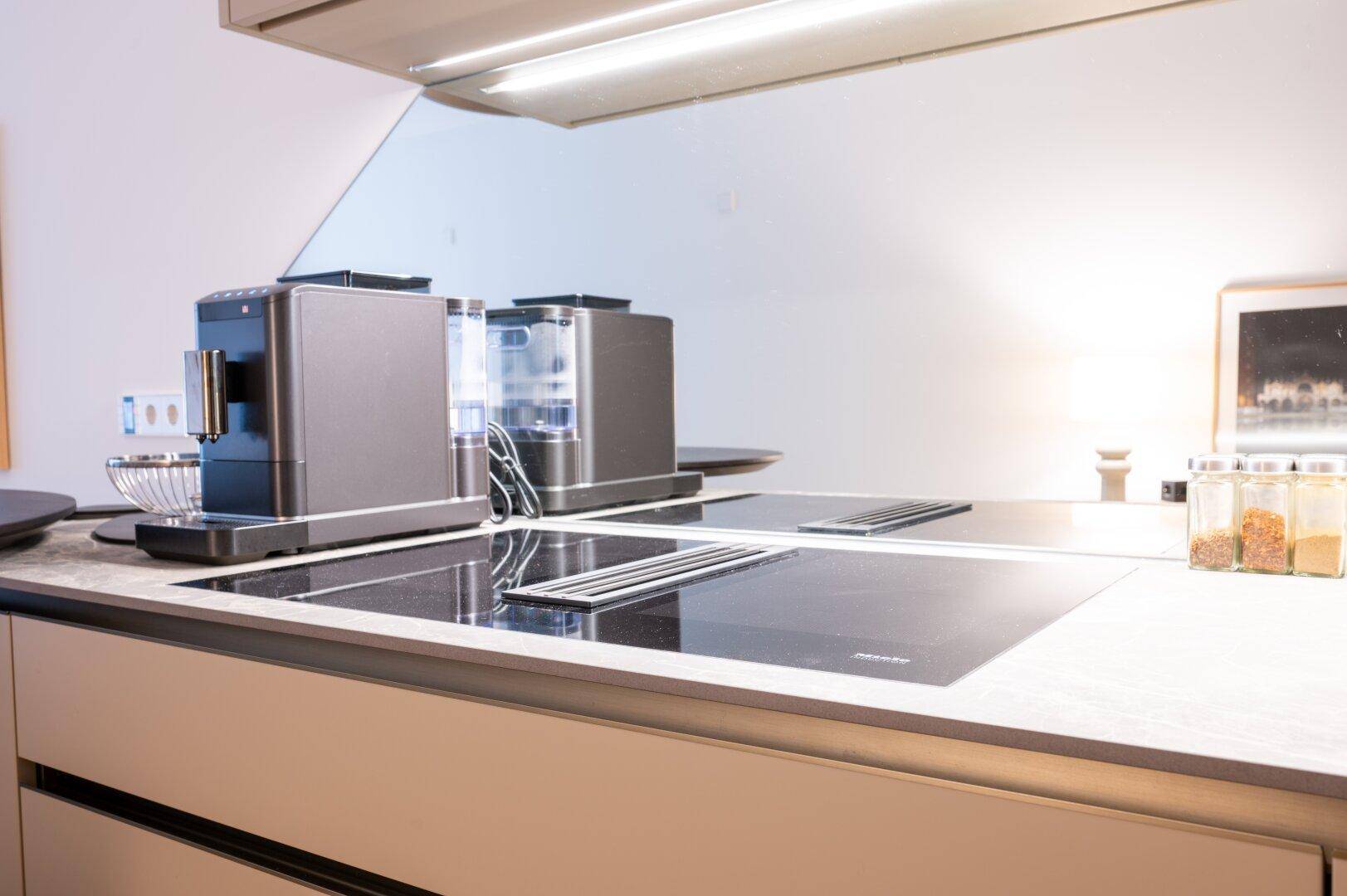 Moderne Küchenzeile mit Induktionskochfeld, integriertem Dunstabzug und Kaffeemaschine.