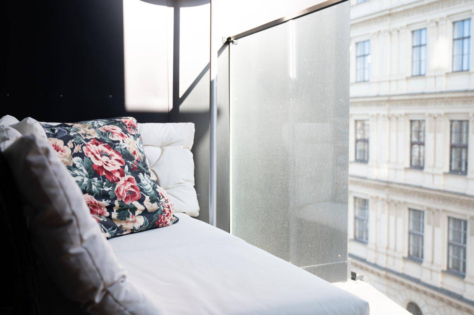 Gemütliche Liege am Fenster mit Blick auf die Stadt und dekorativem Kissen.