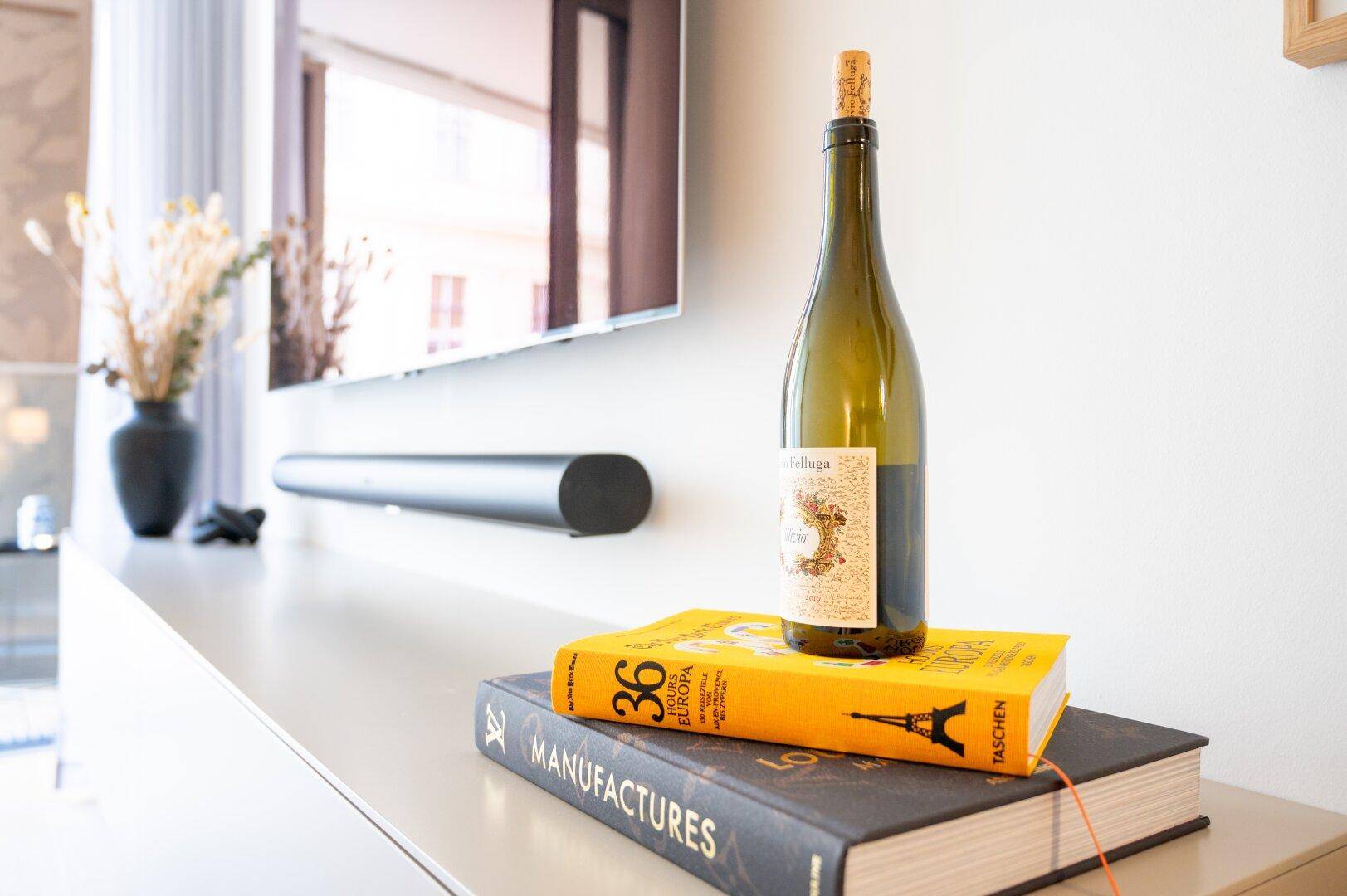 Detailaufnahme von Dekoration auf einem modernen TV-Möbel mit Weinflasche und Büchern.