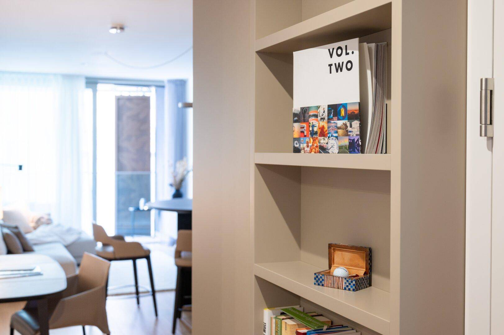 Integriertes Bücherregal im offenen Wohnbereich mit Blick auf den Essbereich und Balkon.