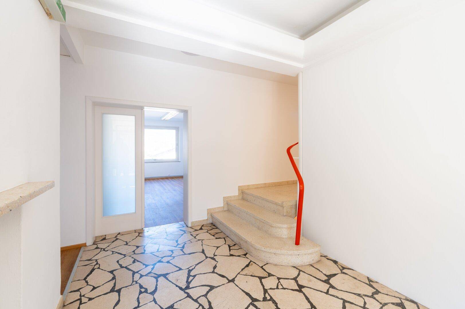 Heller Eingangsbereich mit Terrazzoboden, einer geschwungenen Treppe und weiß gestrichenen Wänden.