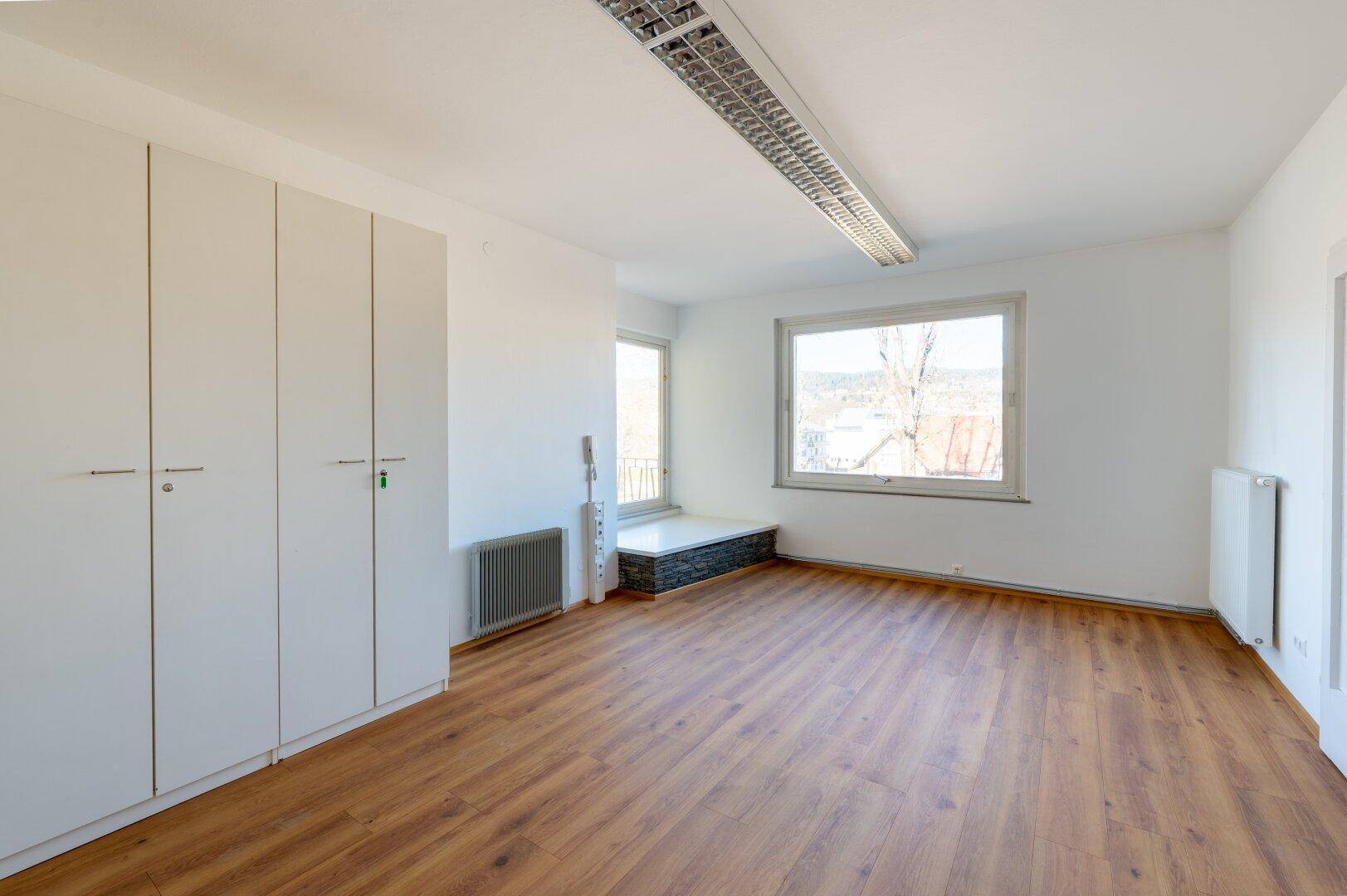 Geräumiges Büro mit Laminatboden, Einbauschränken und großen Fenstern mit Ausblick.