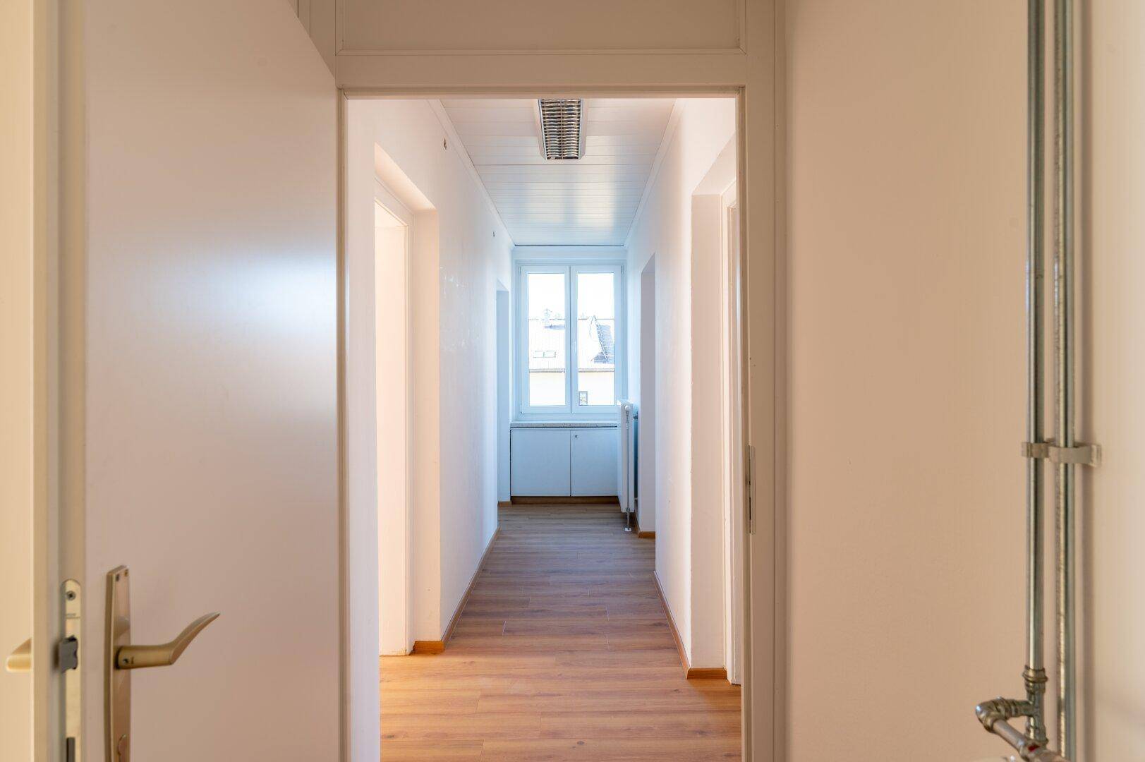 Heller Flur mit Laminatboden, der zu einem Fenster am Ende des Ganges führt.