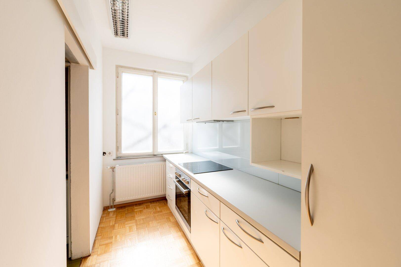 Kleine, helle Küchenzeile mit weißen Schränken, Induktionskochfeld und Fenster.