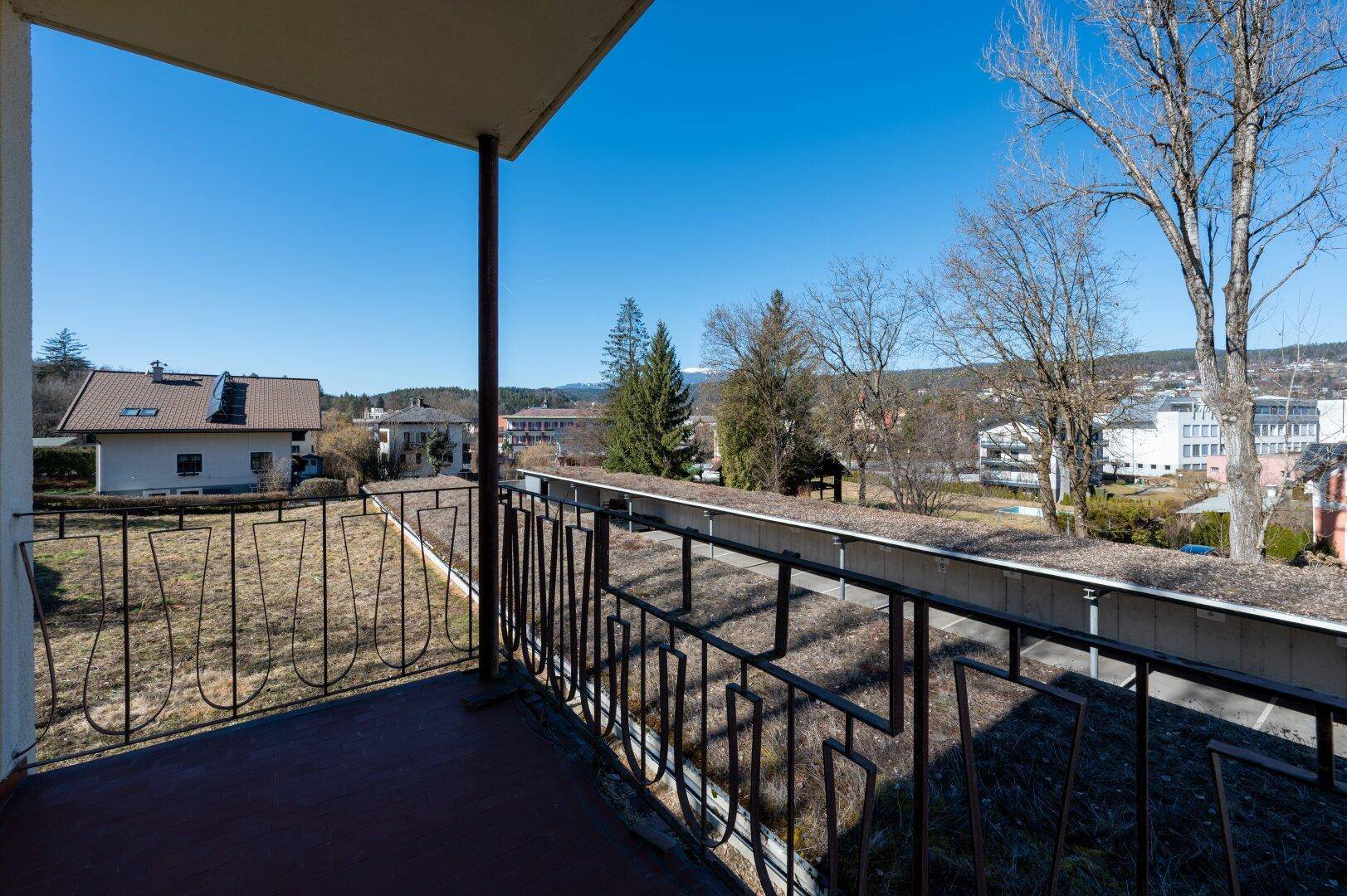 Balkon mit Metallgeländer und weitem Blick über die Umgebung und bewaldete Hügel.