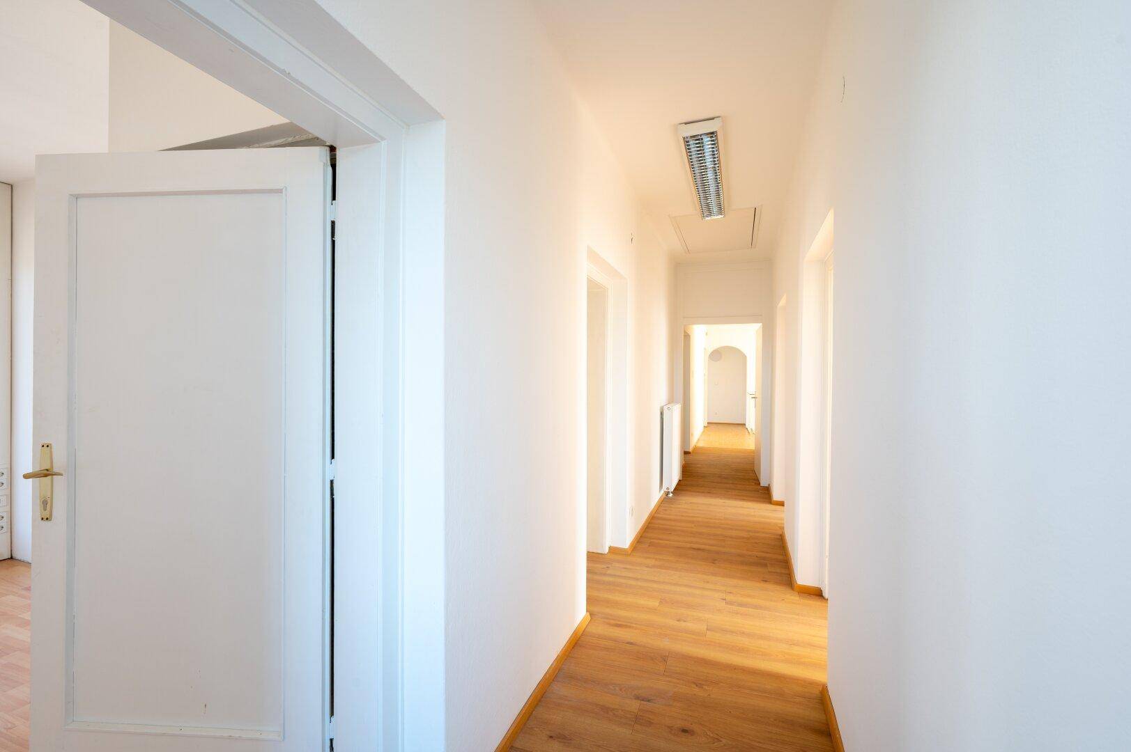 Langer, heller Flur mit Laminatboden und mehreren Türen, der zu weiteren Räumen führt.