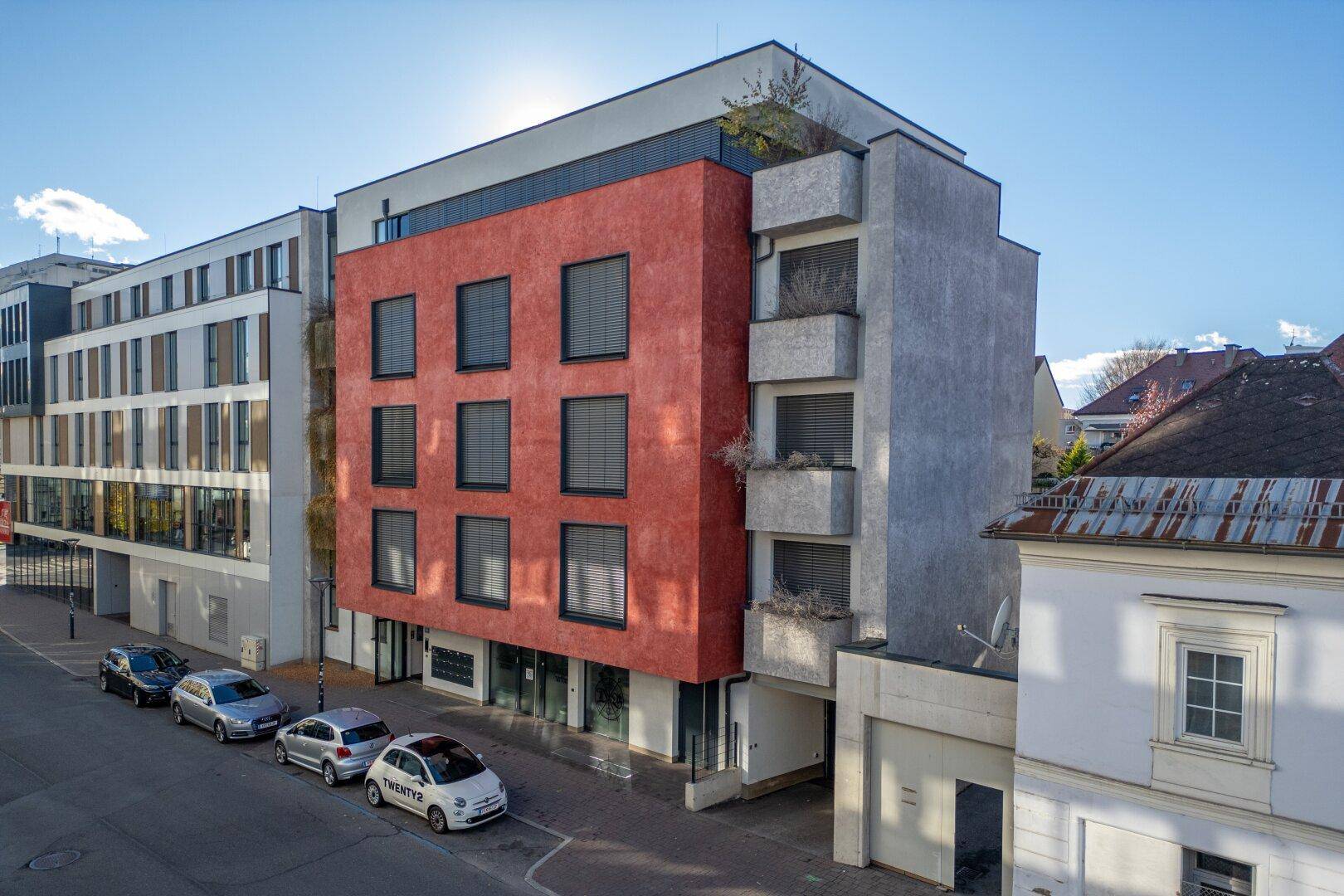 Modernes Wohngebäude mit roter Fassade, Balkonen und großen Fenstern.