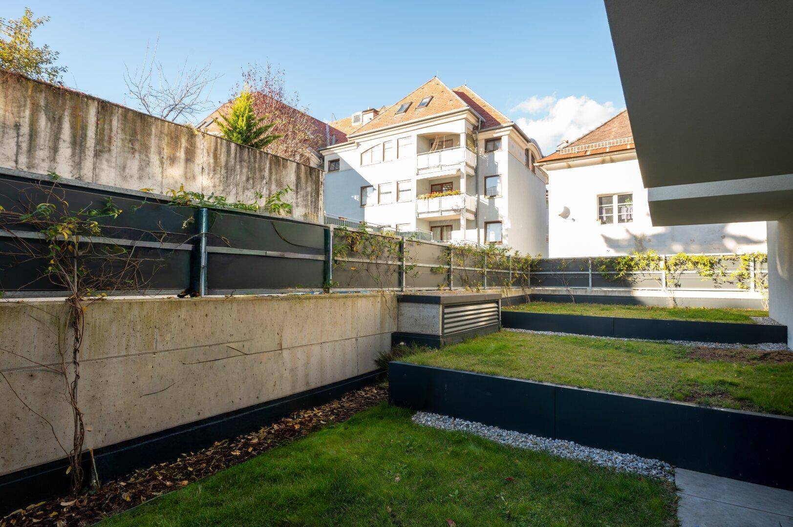 Gepflegter Gartenbereich mit Rasenflächen und Betonmauern im Innenhof.