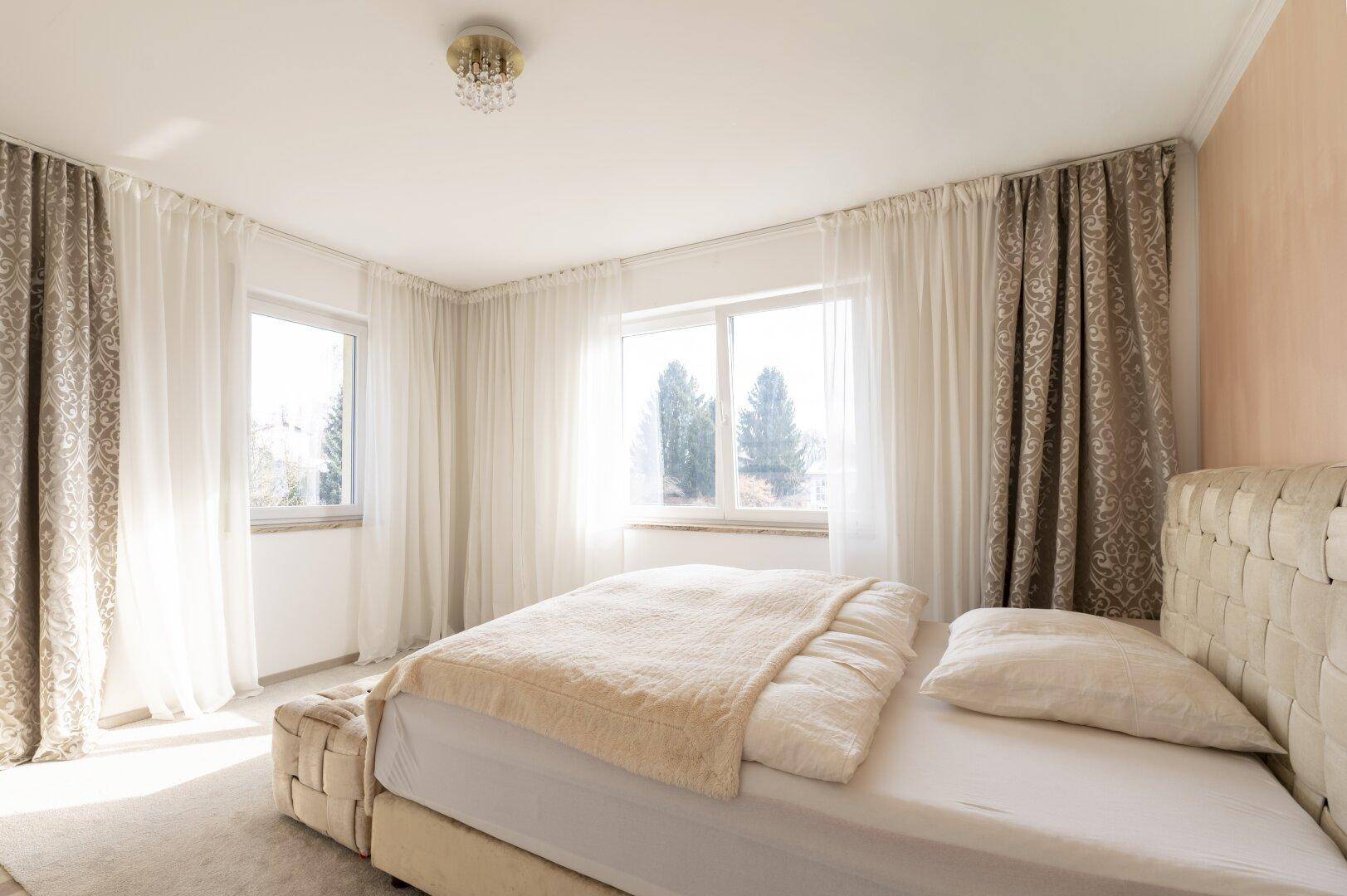 Helles Schlafzimmer mit großem Doppelbett und mehreren Fenstern, die viel Licht hereinlassen.