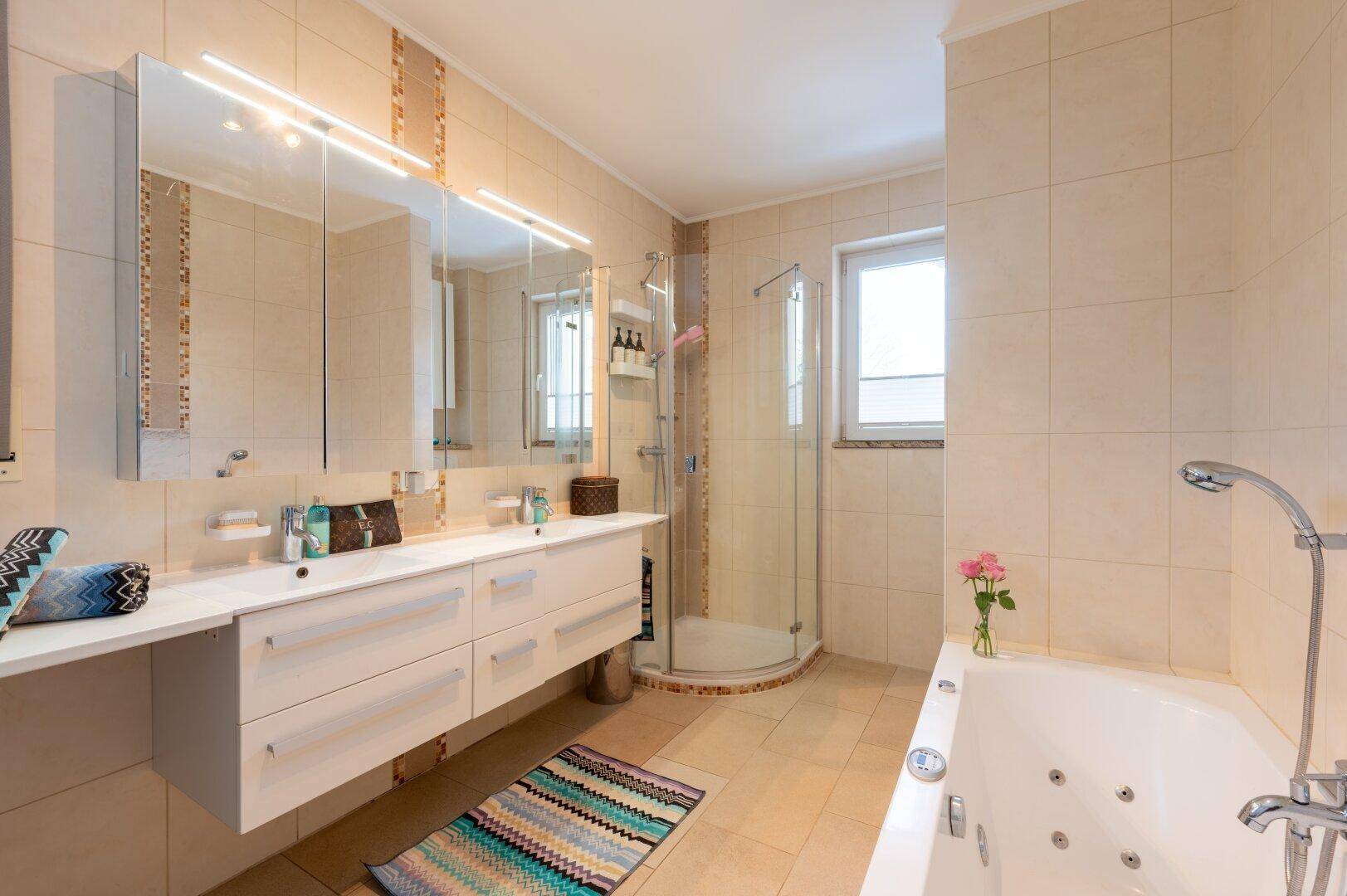 Helles Badezimmer mit moderner Ausstattung, Whirlpool-Badewanne, Dusche, Doppelwaschbecken und Fenster.