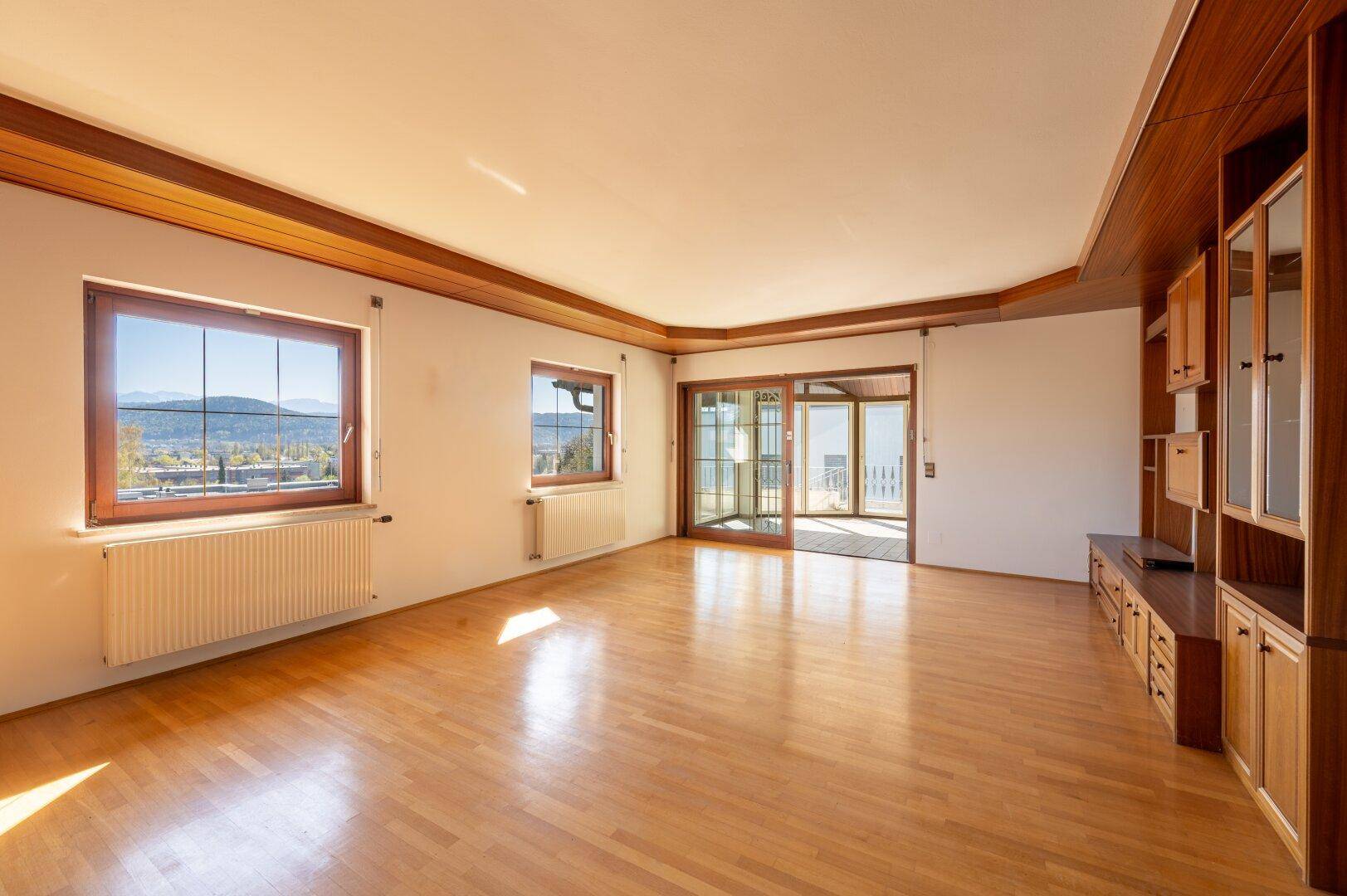 Lichtdurchflutetes Wohnzimmer mit Holzboden und Zugang zu einem Balkon, bietet Bergblick.