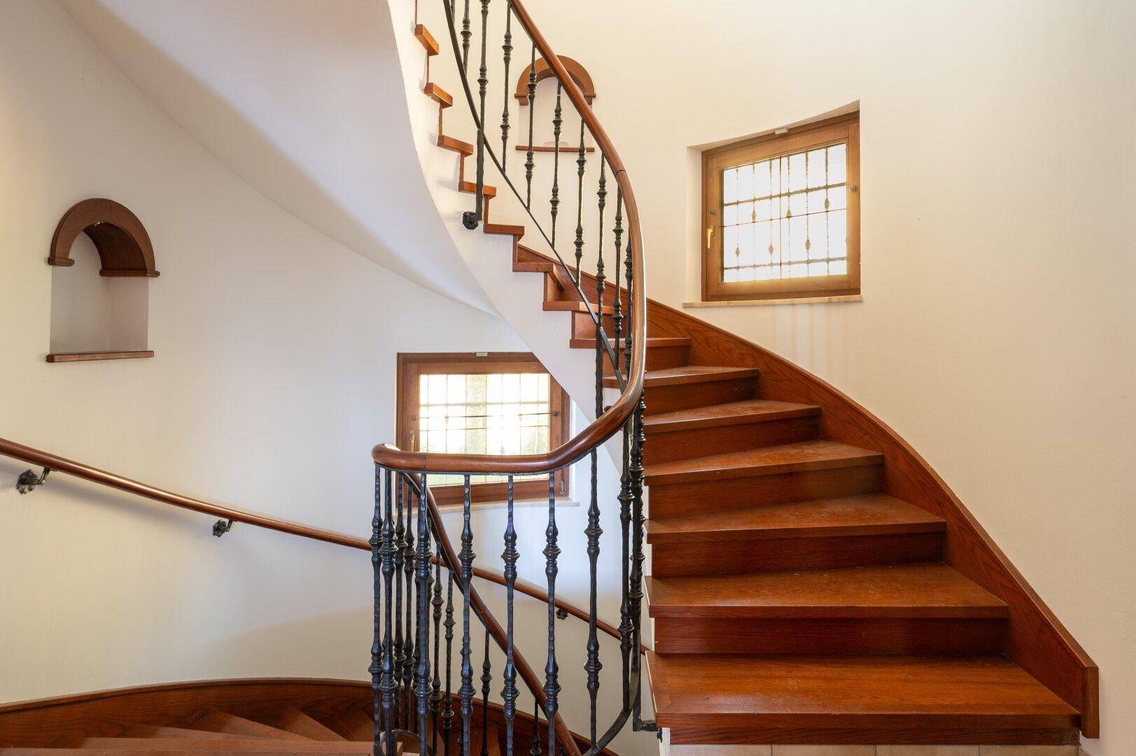 Elegante Holztreppe mit schmiedeeisernem Geländer, die die verschiedenen Etagen verbindet.