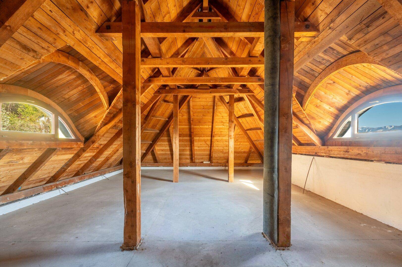 Geräumiger Dachboden mit sichtbaren Holzbalken und Rundfenstern, ideal für einen Ausbau.